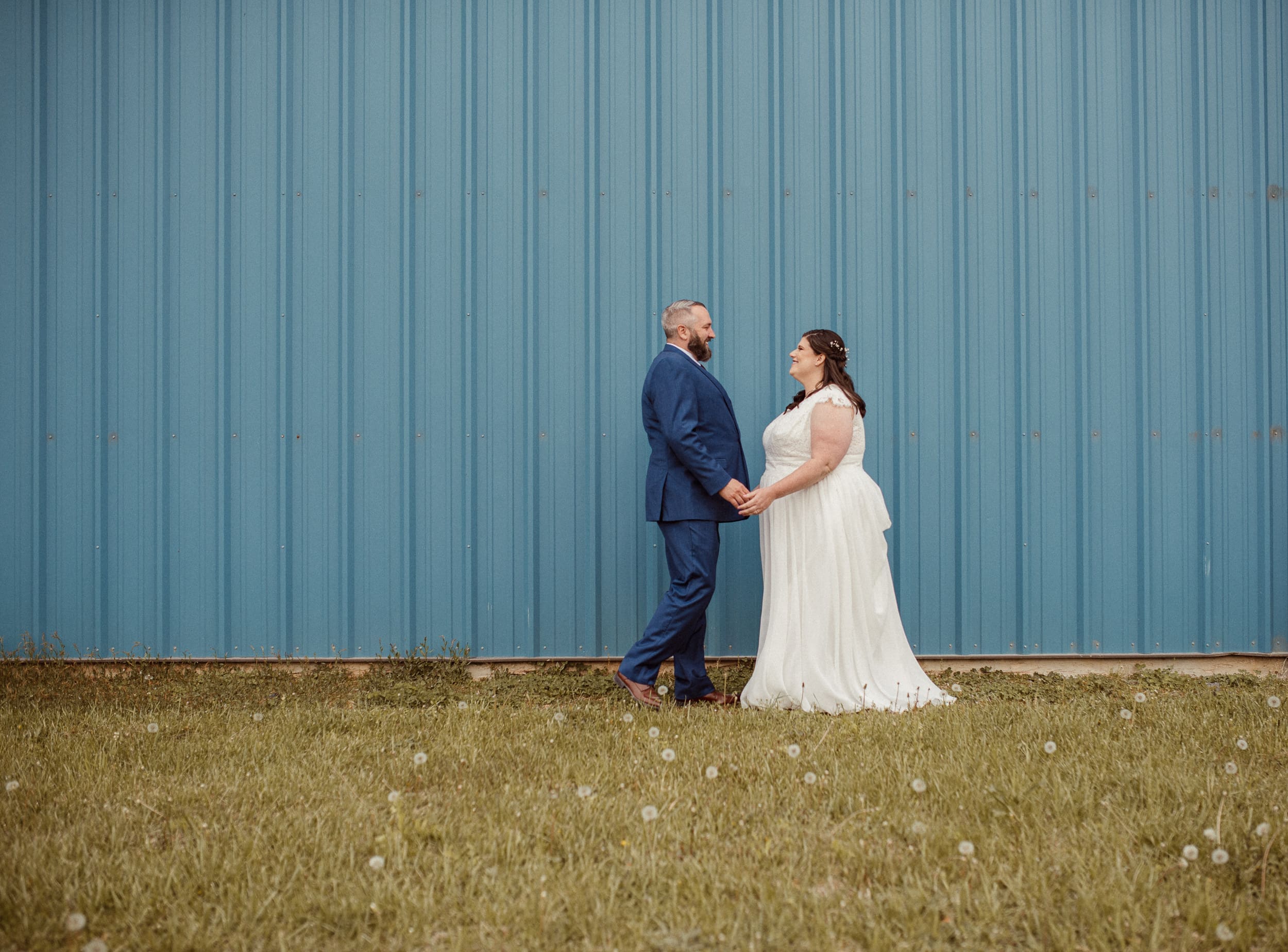 Bride and groom holding hands in front of blue wall for modern wedding portrait