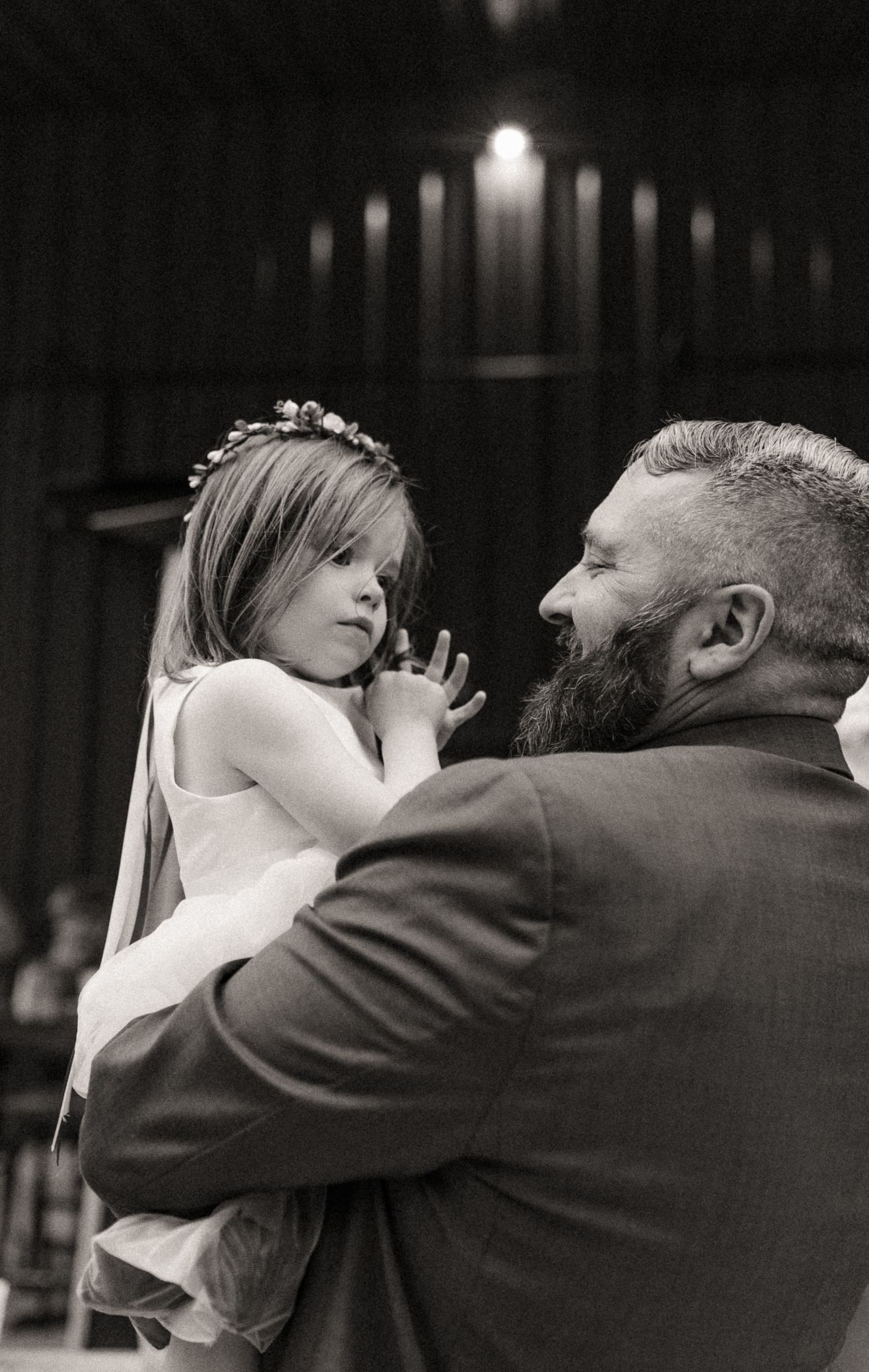 Black and white photo of groom holding child during emotional moment at intimate wedding reception. 