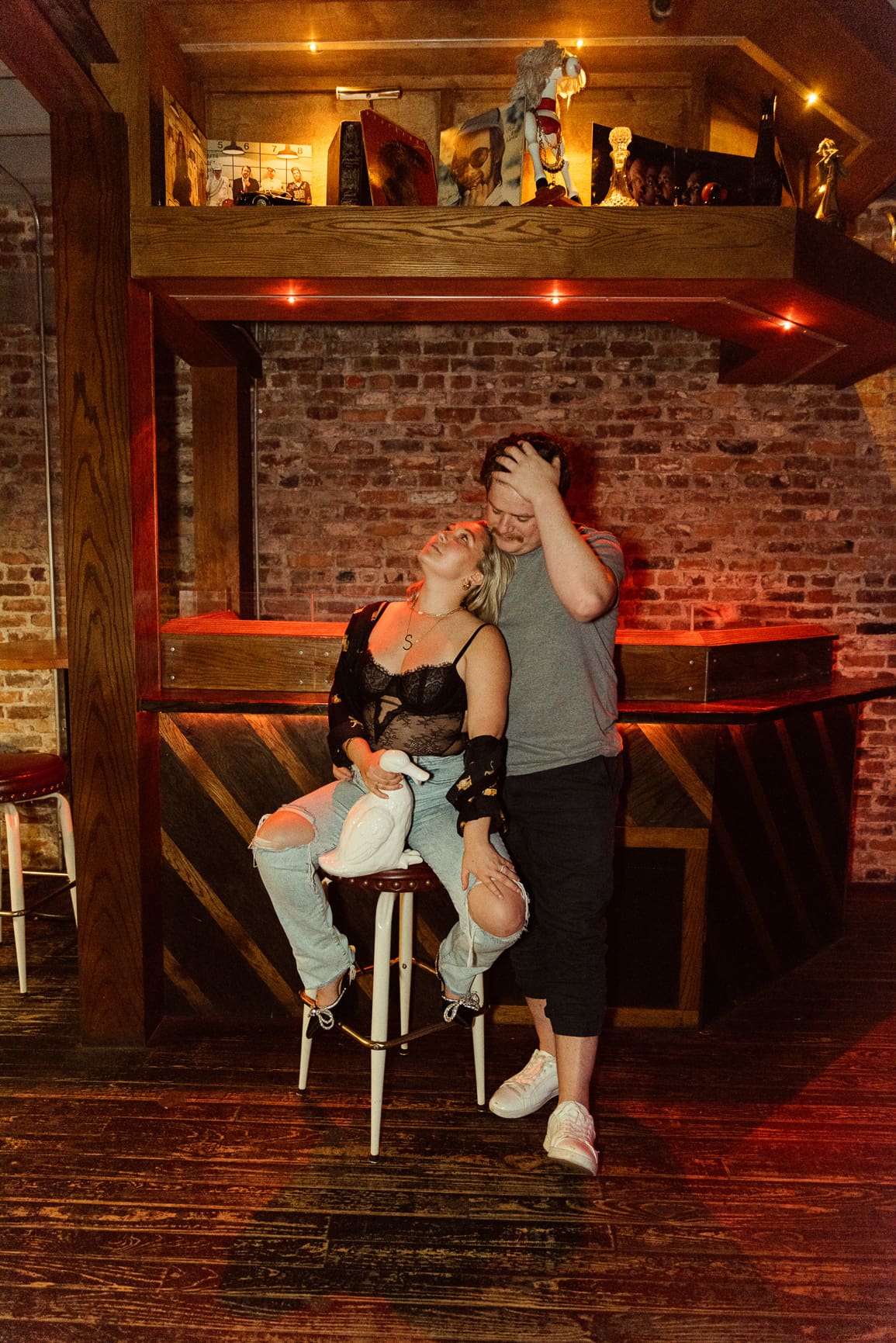 Couple in bold mixed-style outfits for engagement photos in a moody bar setting with warm lighting