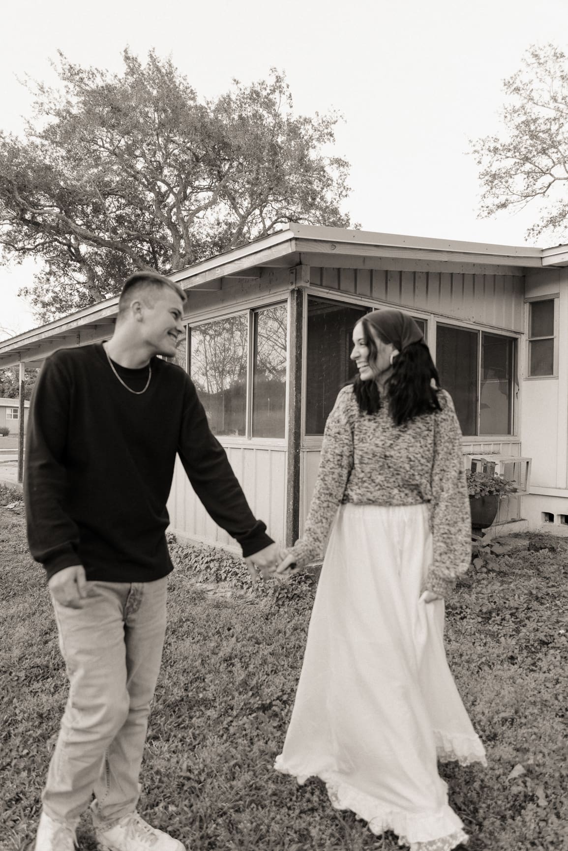 Couple wearing relaxed neutral outfits for engagement photos in a cozy outdoor setting