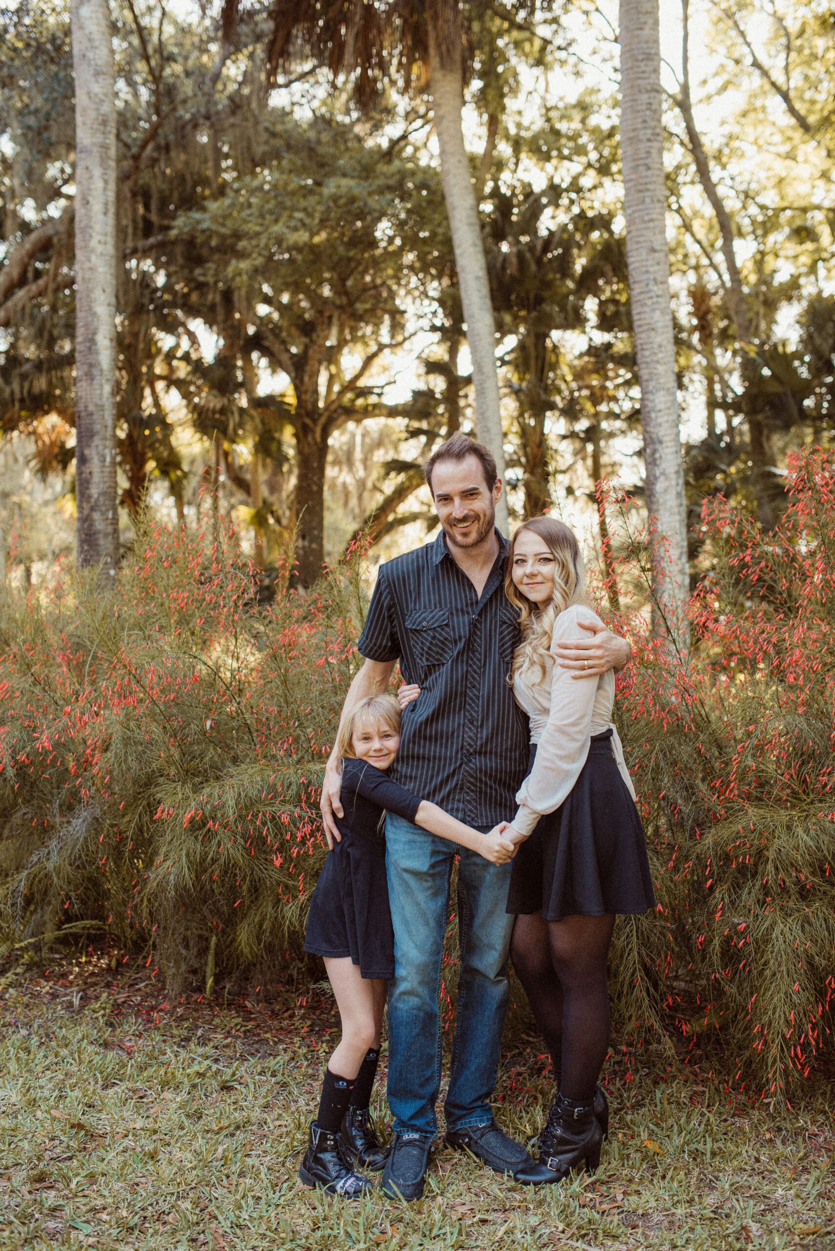 Family wearing darker coordinated outfits with texture in a garden setting with red florals. 