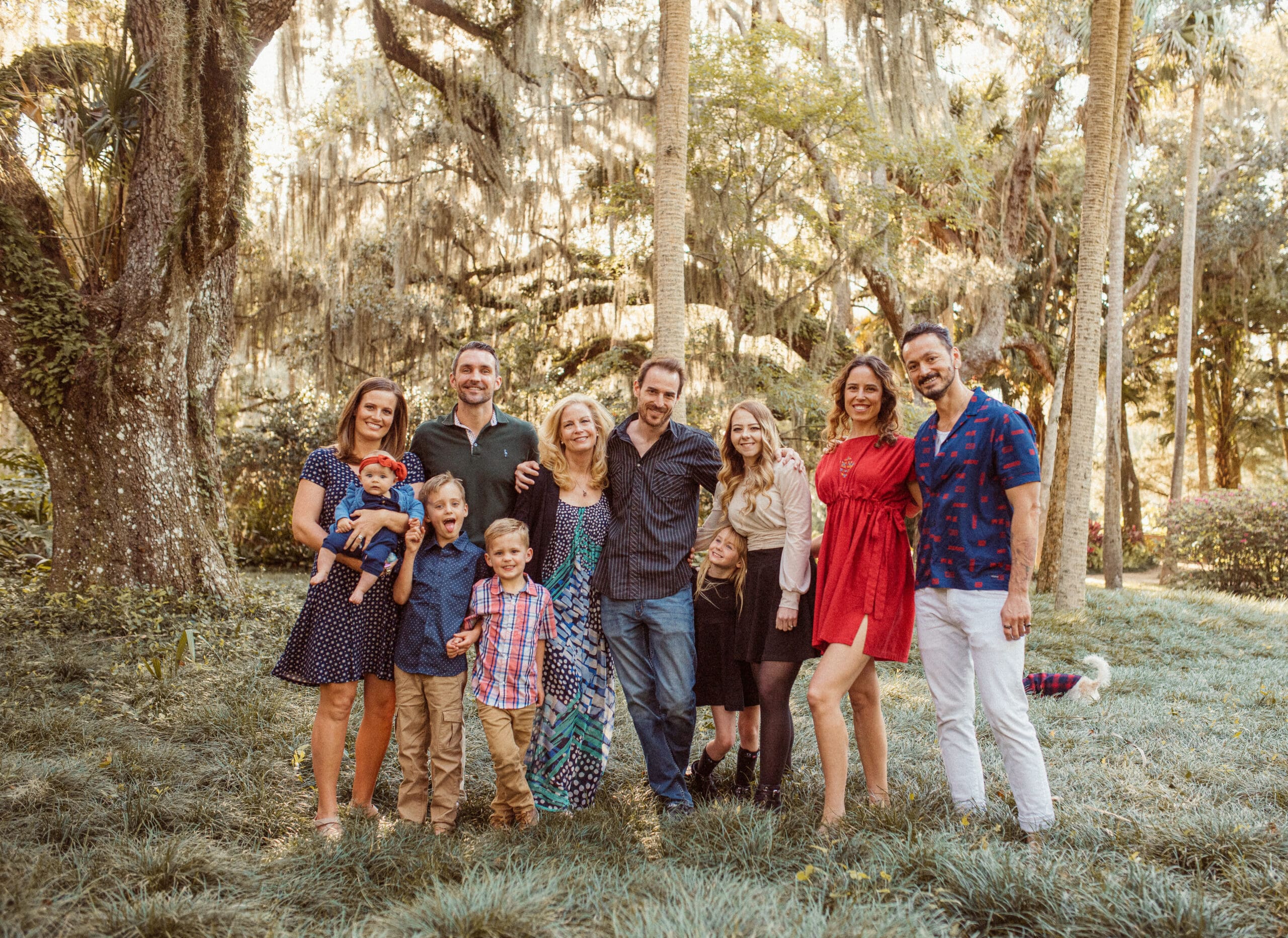 Extended family group photo with coordinated outfits in a mix of colors and textures outdoors. 