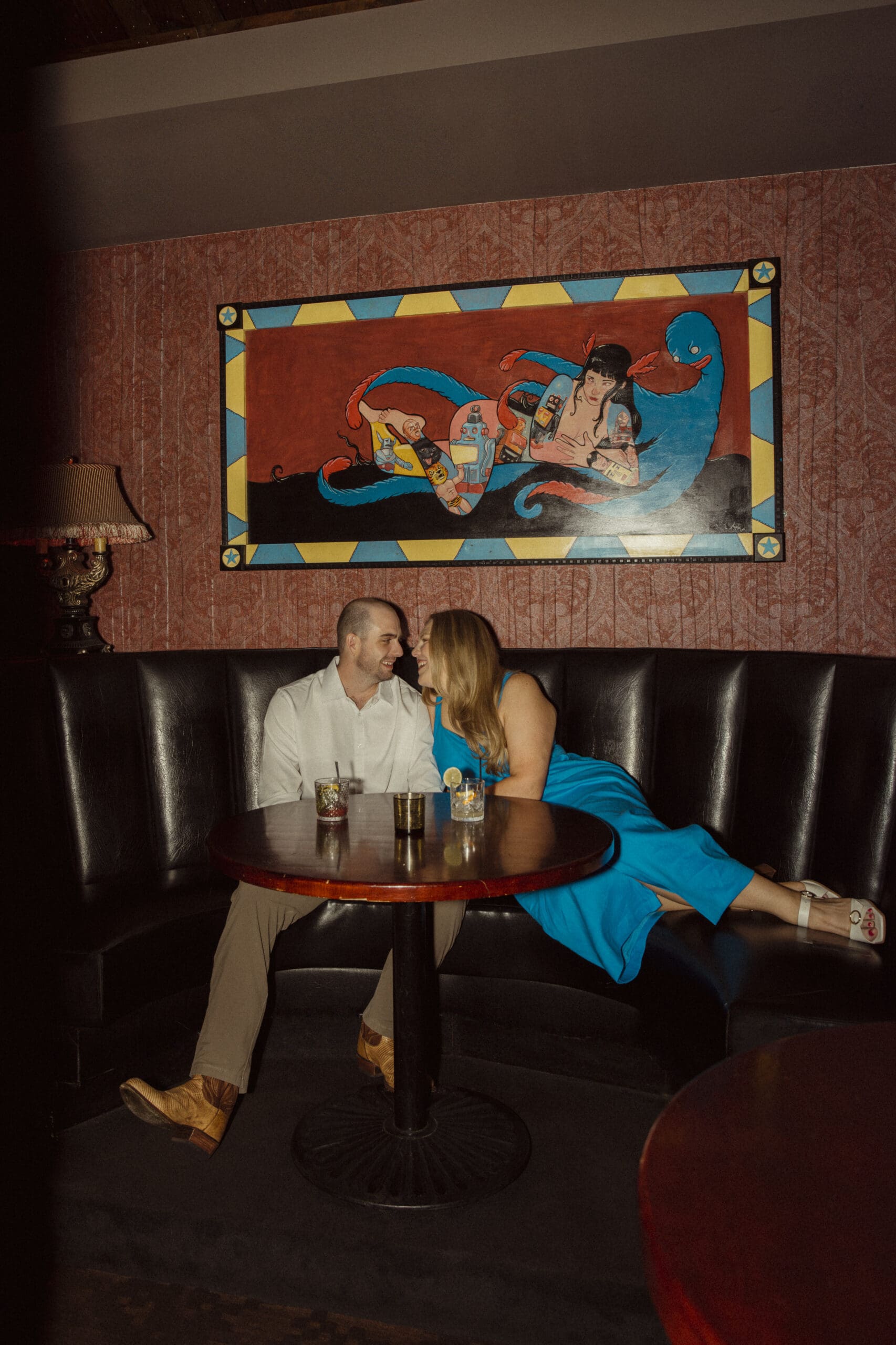 Couple dressed in elevated date night outfits for engagement photos in a moody lounge setting