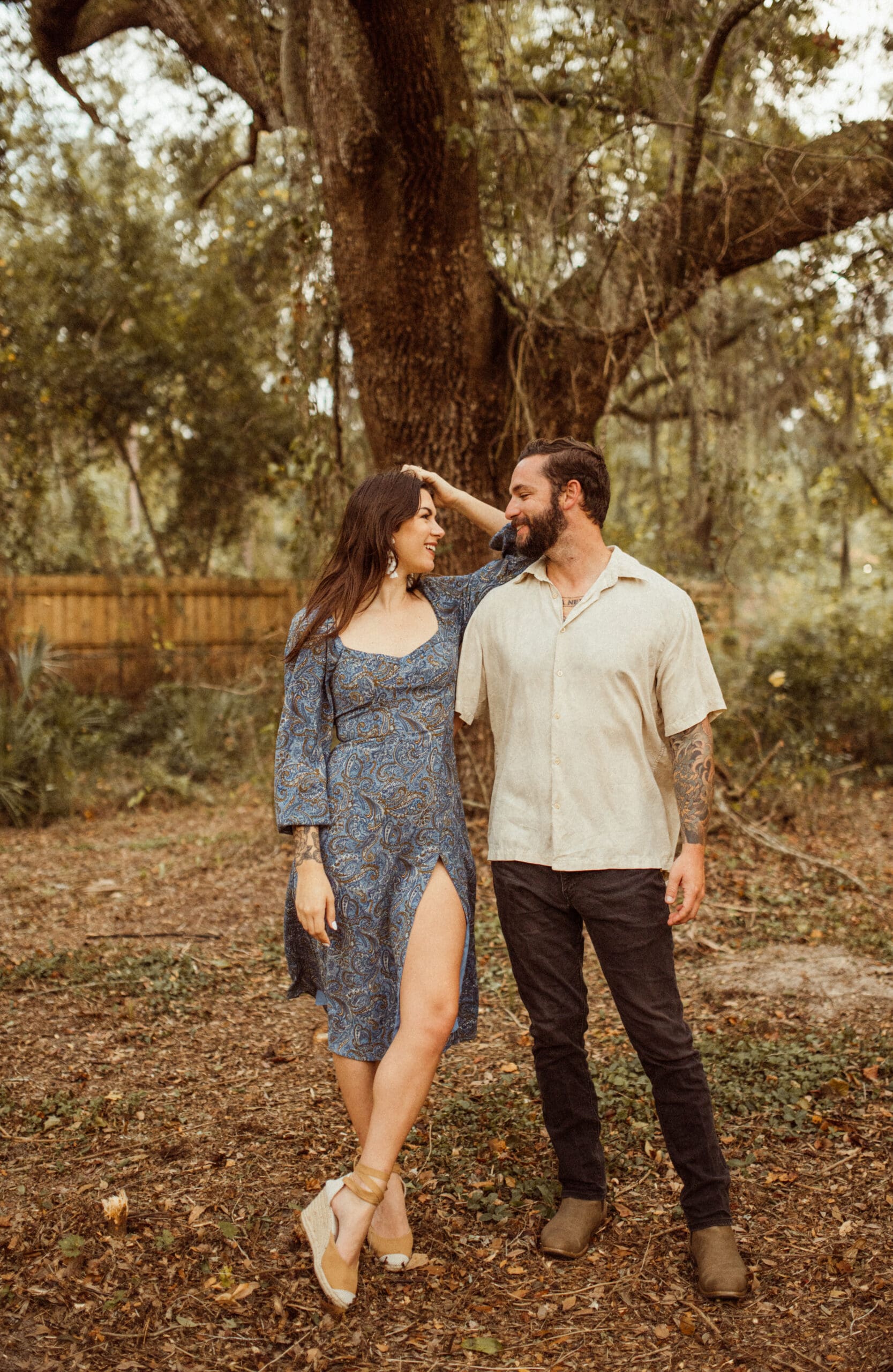 Couple walking under oak trees in earth toned outfits creating a grounded and romantic engagement session look. 