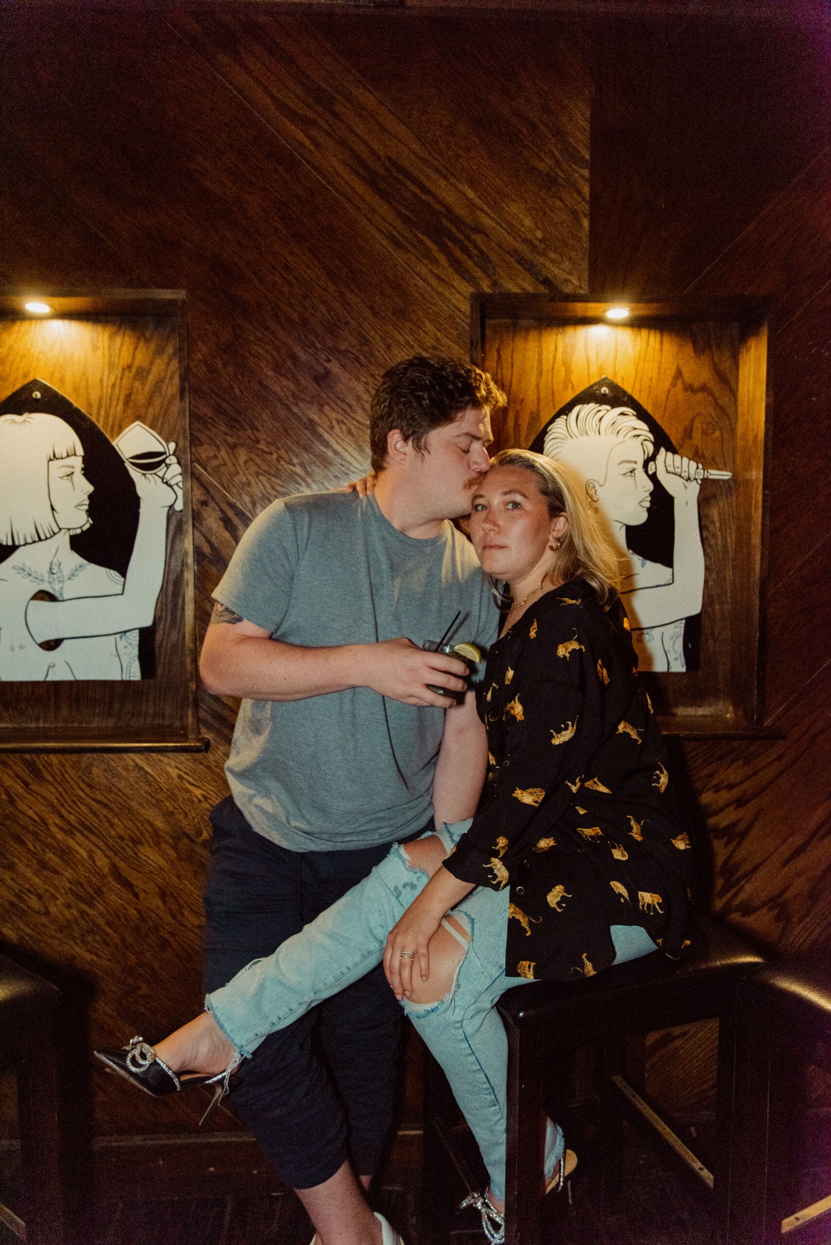 Couple at bar sharing intimate candid moment with drink in hand, playful date night engagement session indoors. 