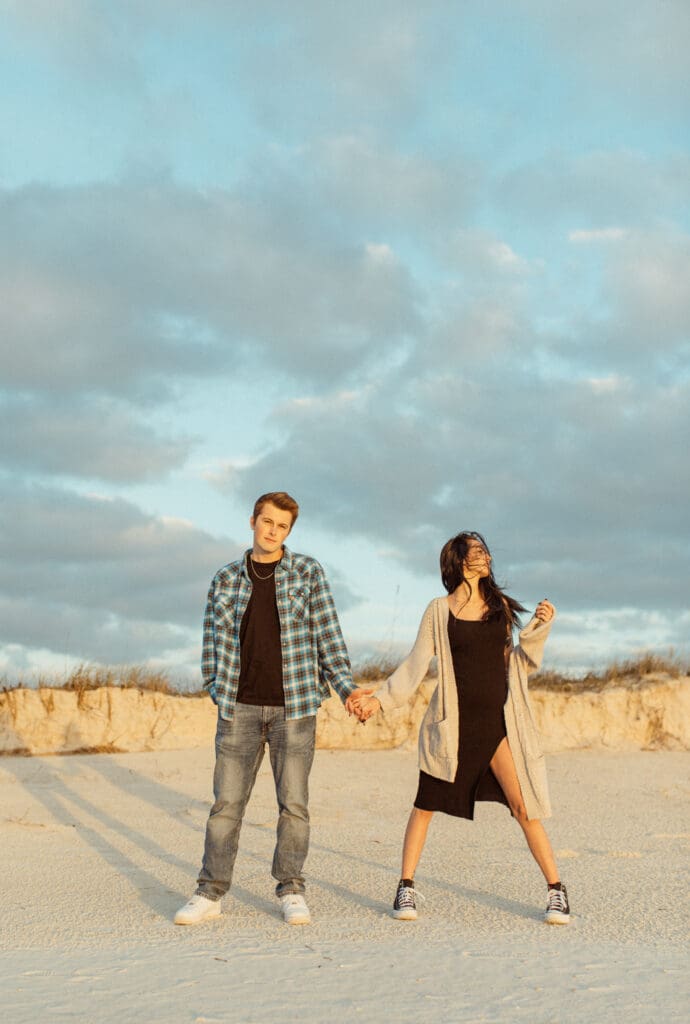 Couple walking on beach with windblown hair, playful engagement photos with movement and carefree vibe. 