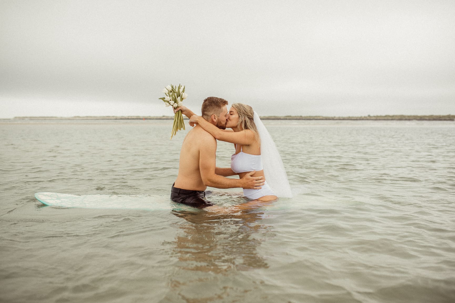 Bride and groom embracing on a surfboard in water at Vilano Beach after their elopement. 