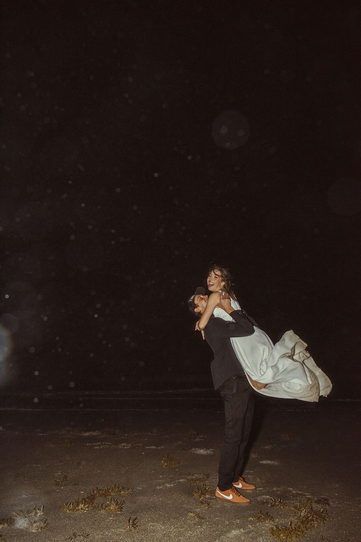 Playful nighttime elopement photo of couple with flash photography on the beach. 