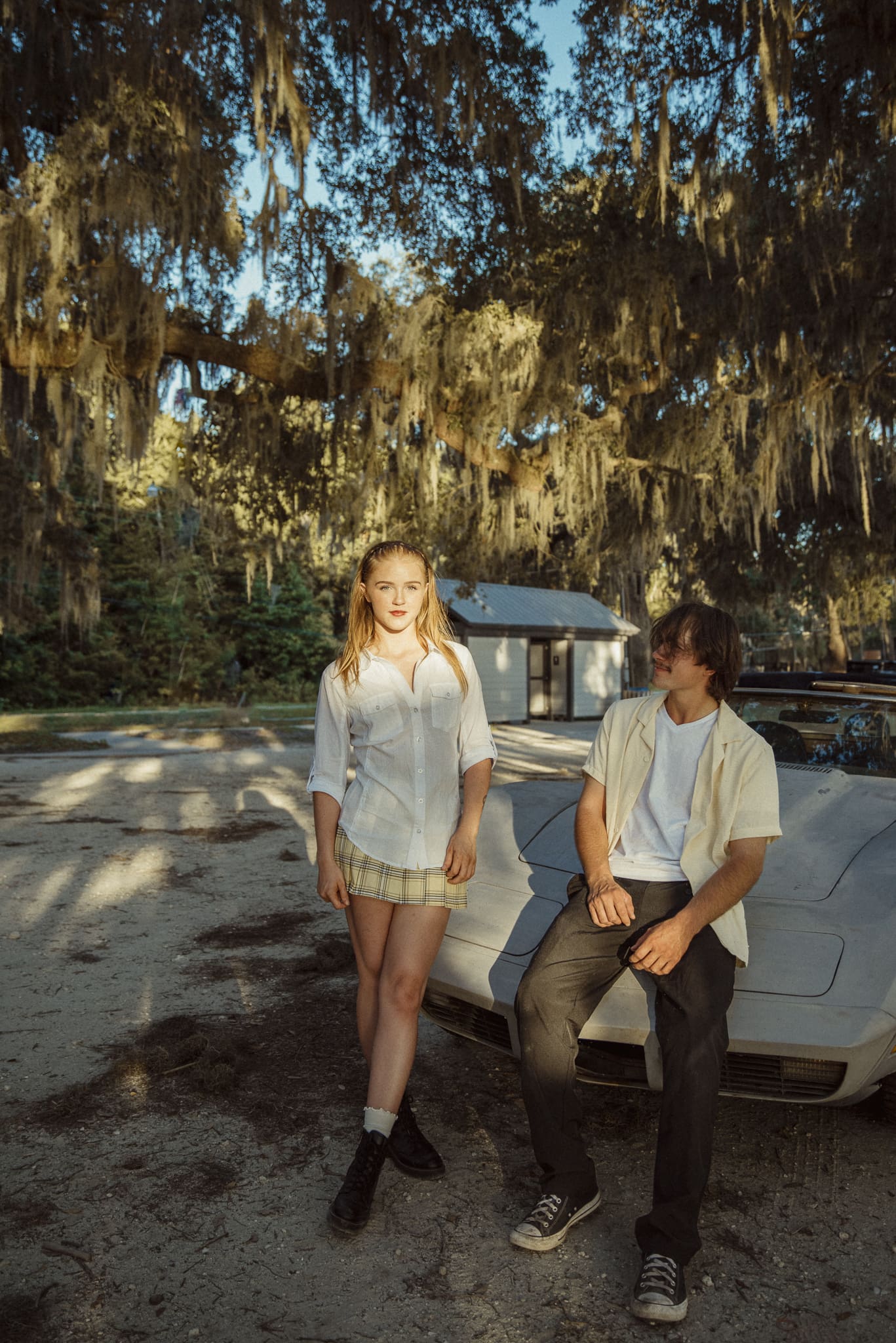 Couple posing by vintage car under oak trees with soft editorial styling, natural light and relaxed romantic aesthetic. 