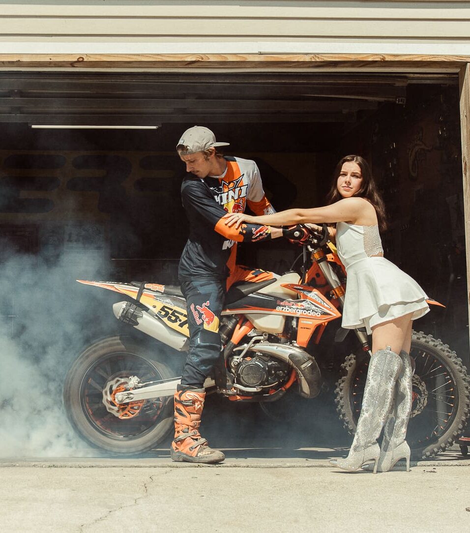 Editorial couple session with dirt bike and contrasting fashion styling in St. Augustine, woman in white dress and silver glitter boots, man in motocross gear.
