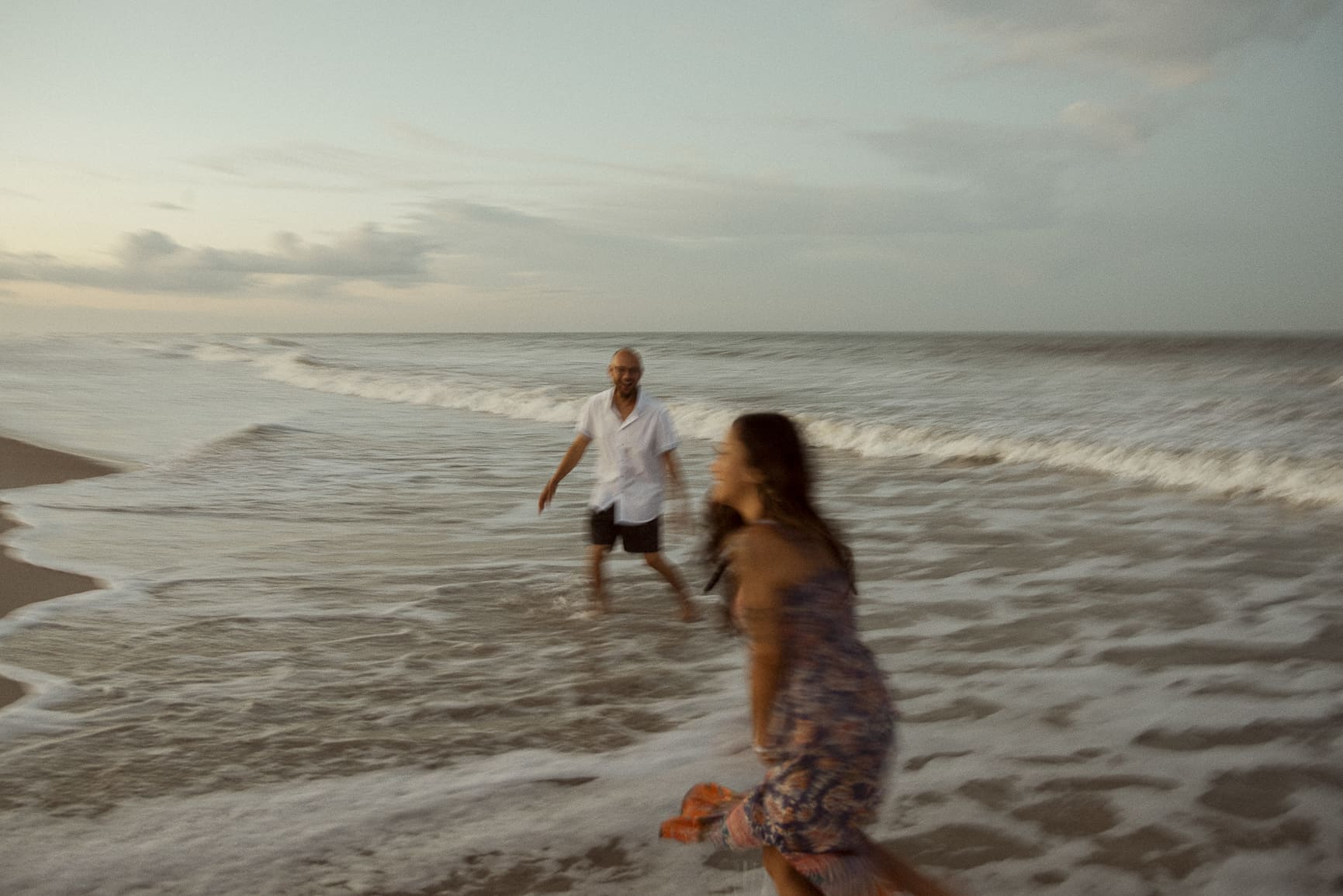couple running into the ocean with motion blur, playful beach engagement session capturing movement and carefree energy. 