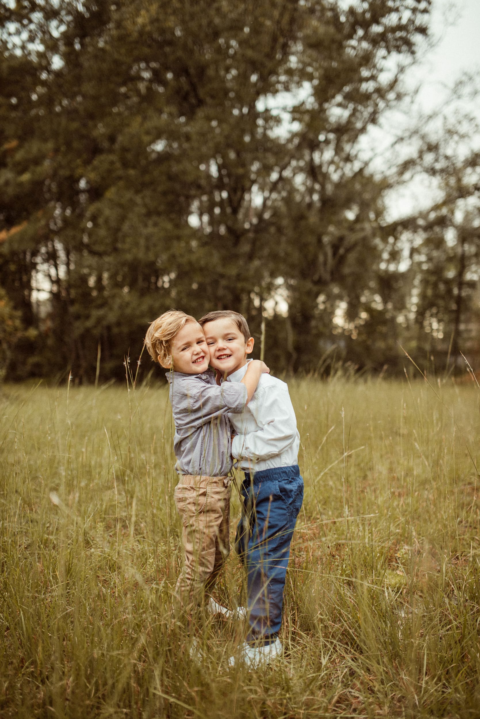 Children hugging in tall grass during backyard engagement photos in Mandarin, capturing a candid family moment.