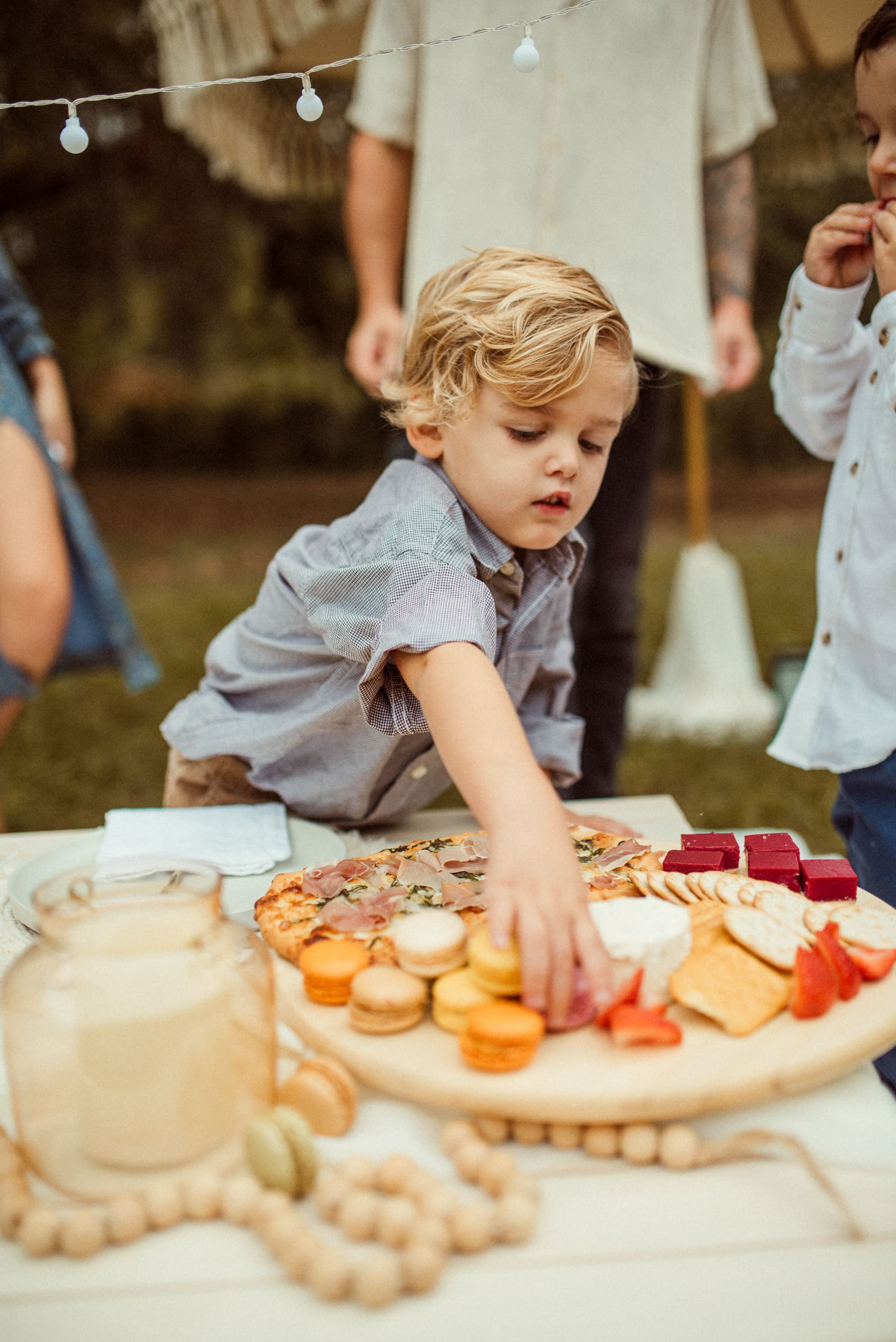 Young child reaching for food at a picnic during a backyard engagement session in Jacksonville, Florida.