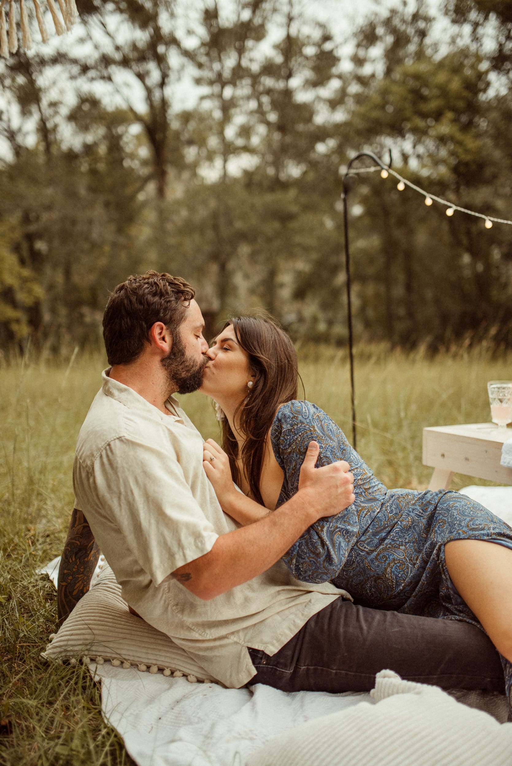 Couple kissing on a blanket during a romantic backyard engagement session.