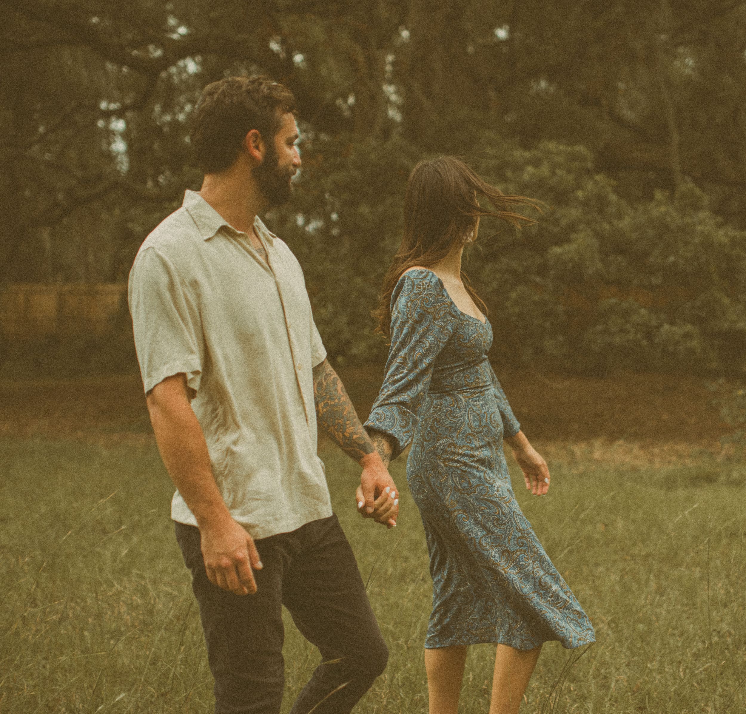 Couple walking hand in hand through a backyard at golden hour during an engagement session in Jacksonville on film.