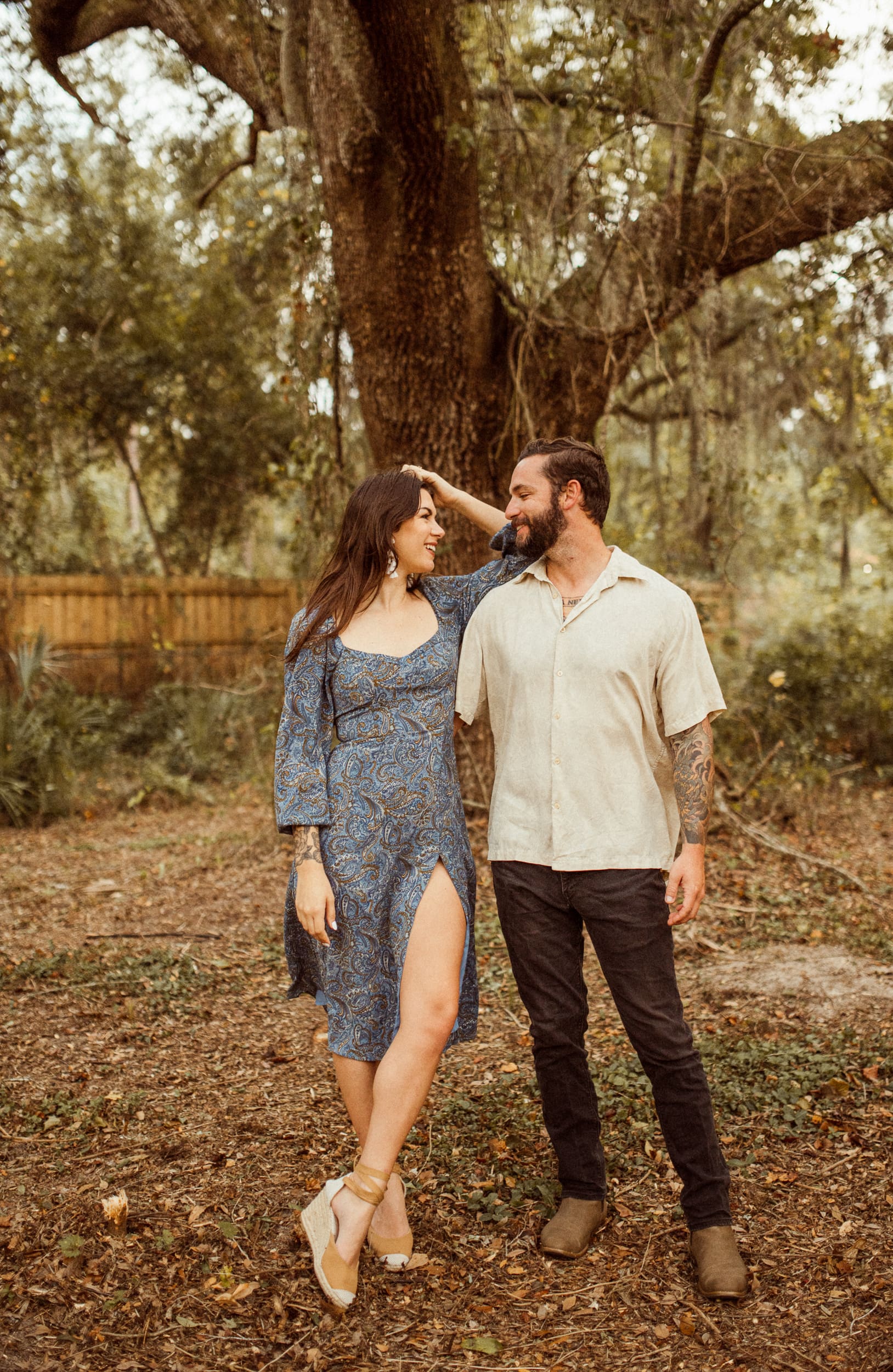 Couple standing together under a large oak tree during a backyard engagement session in Jacksonville, Florida.