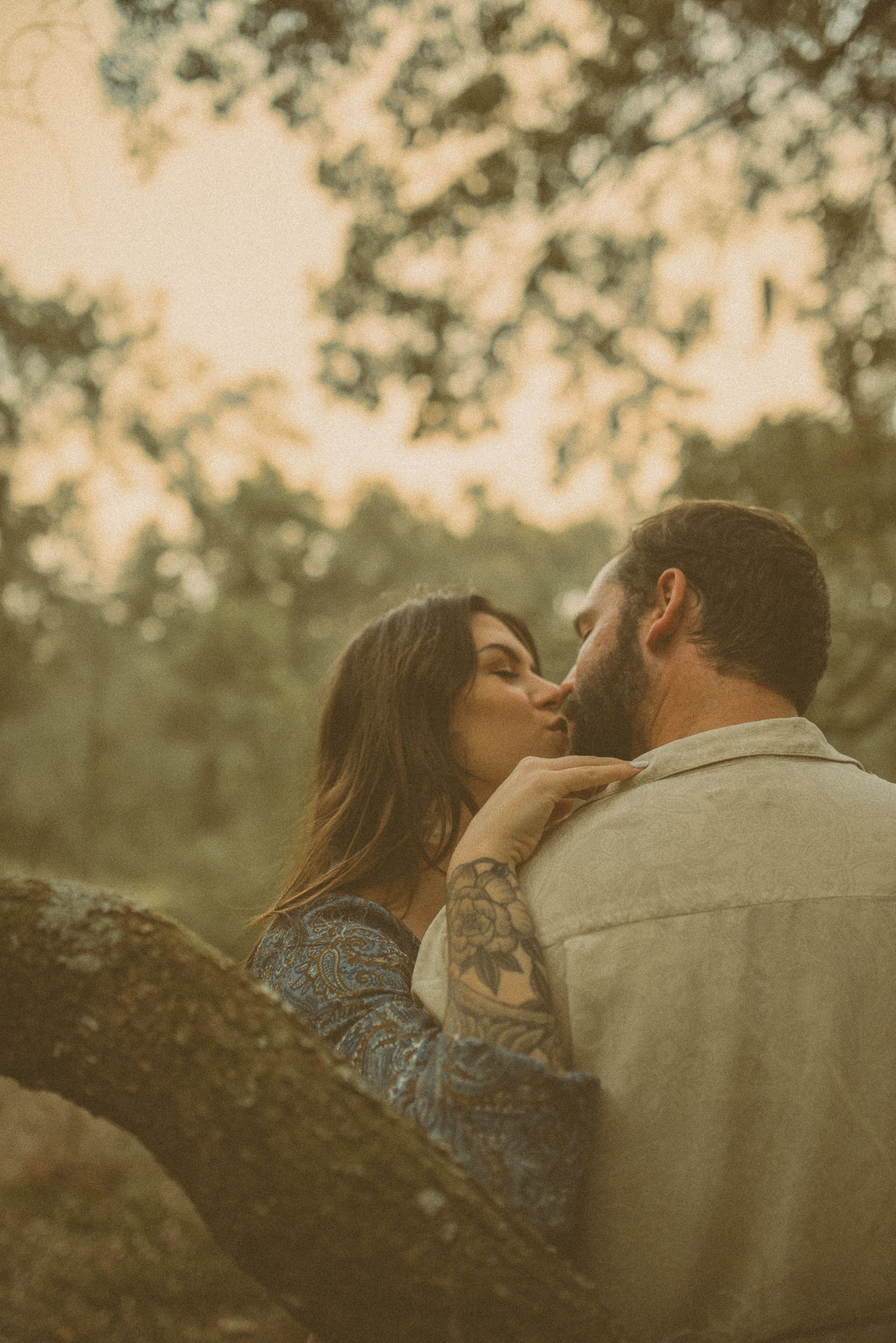 Couple sharing a soft kiss surrounded by trees during a romantic backyard engagement session in Jacksonville, Florida.