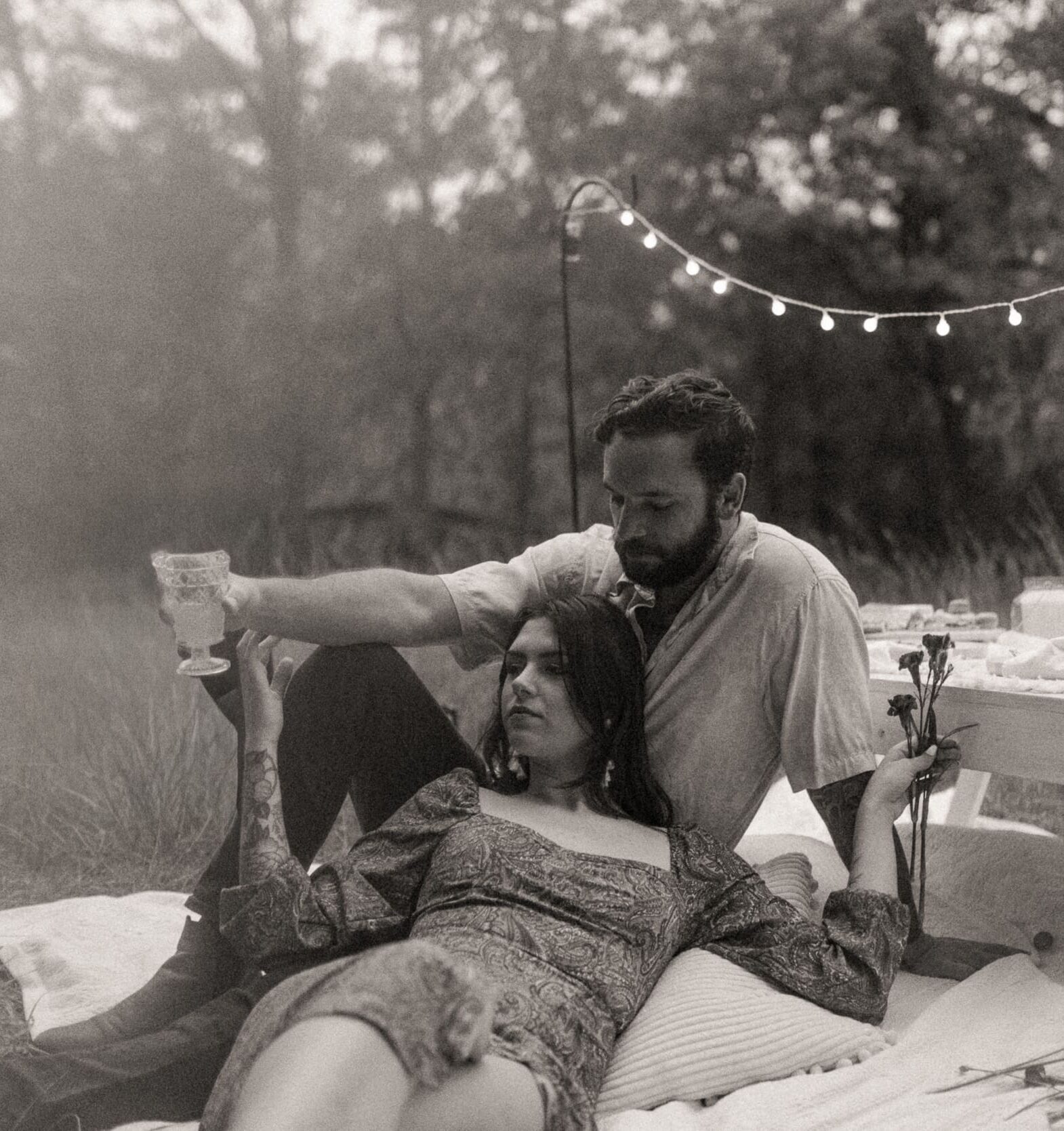 Couple sitting together on a blanket with scattered florals during a romantic backyard engagement session in Jacksonville, Florida.