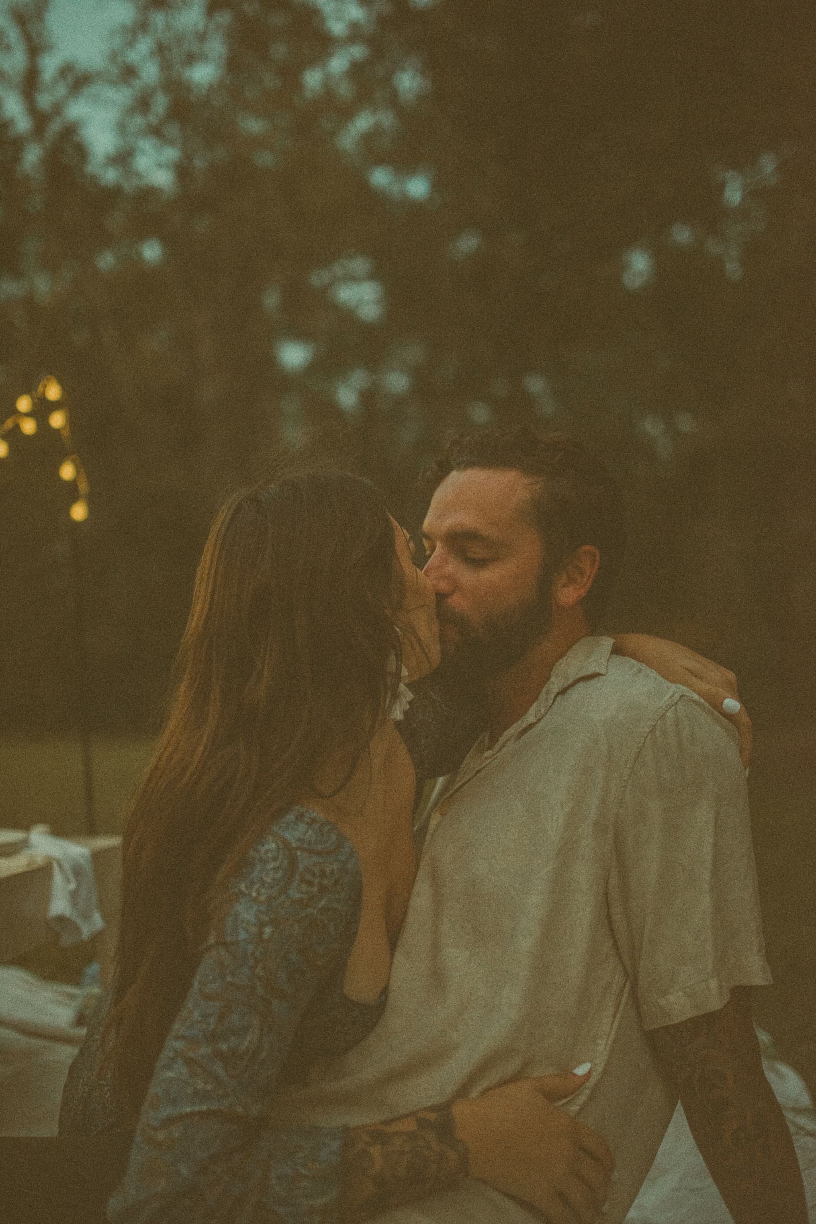 Couple kissing at dusk with soft string lights during a backyard engagement session in Jacksonville, Florida.