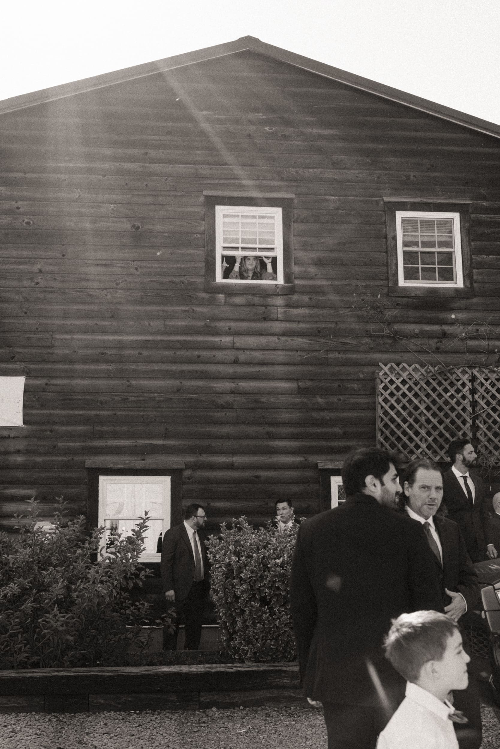 Bride peeking out of chateau window while groomsmen gather below at Parker-Binns Vineyard North Carolina, documentary wedding photography by Brandi Denslow. 