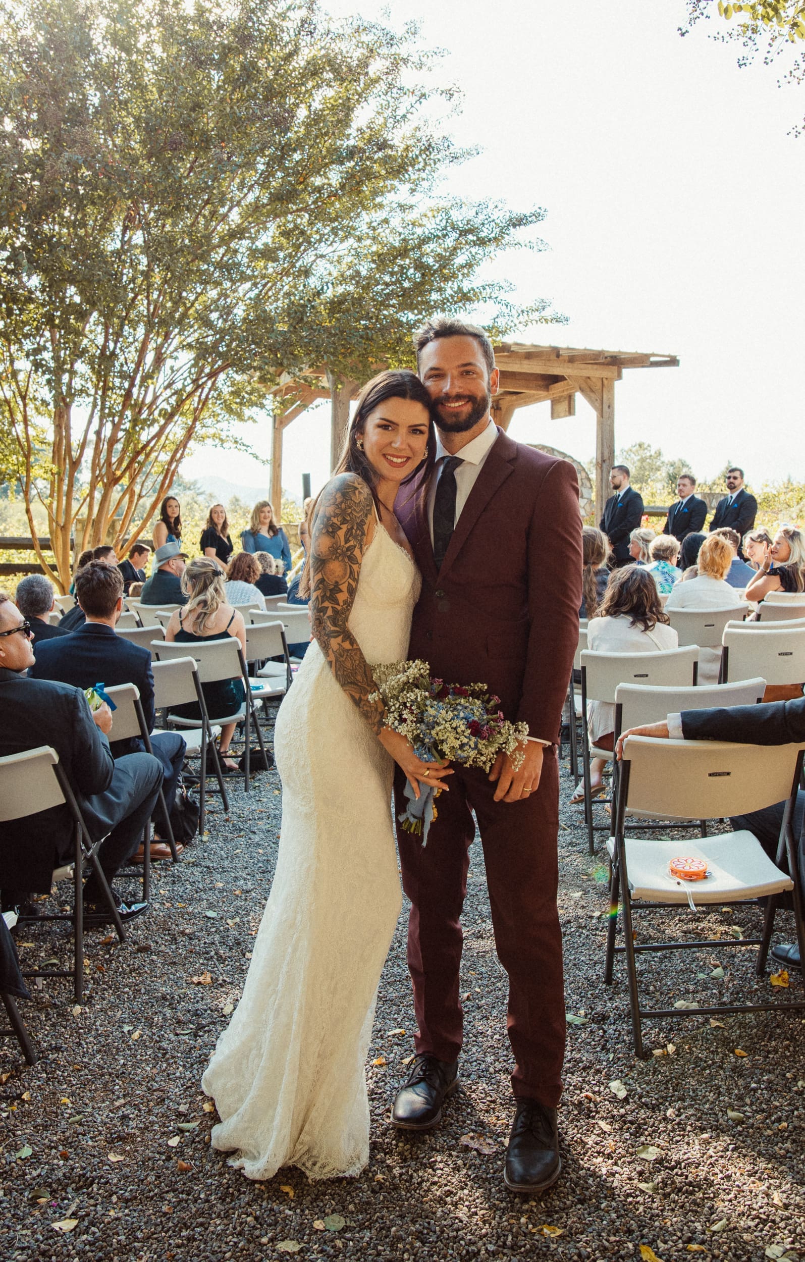 Newly married bride and groom smiling after ceremony at Parker-Binns Vineyard North Carolina with guests behind them, wedding photography by Brandi Denslow. 