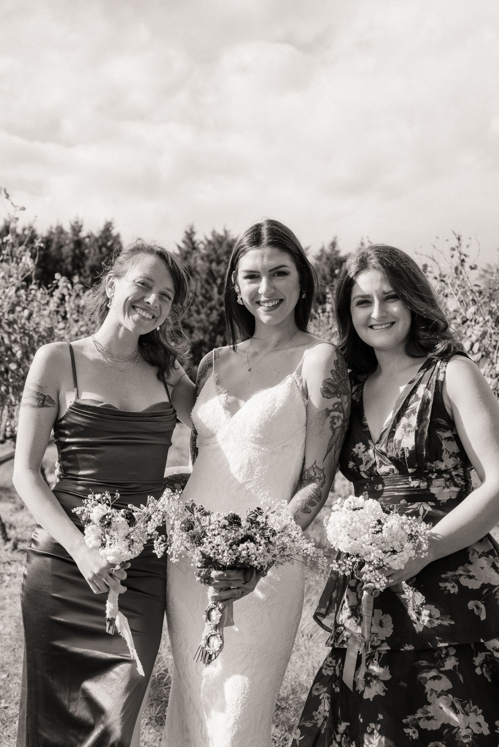 Black and white portrait of bride and two bridesmaids laughing with bouquets at Parker-Binns Vineyard North Carolina. 