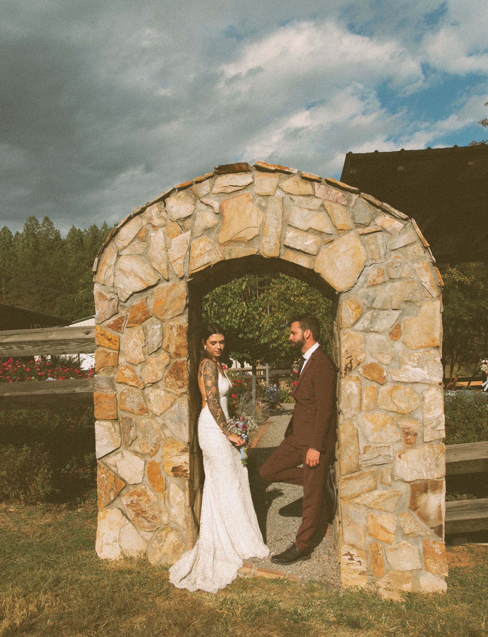 Bride and groom standing inside stone arch at Parker-Binns Vineyard with dramatic stormy sky behind, editorial wedding photography by Brandi Denslow. 