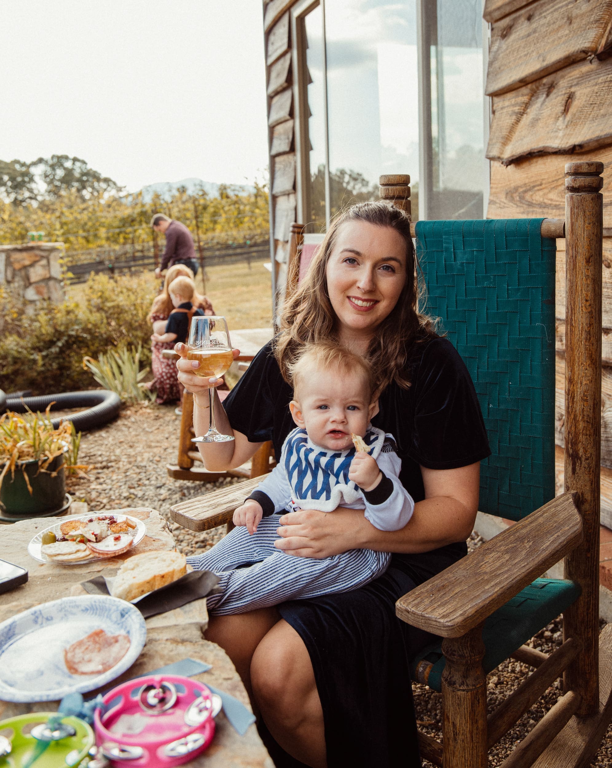 Candid moment of wedding guest holding baby on vineyard porch at Parker-Binns North Carolina, documentary wedding photography by Brandi Denslow. 