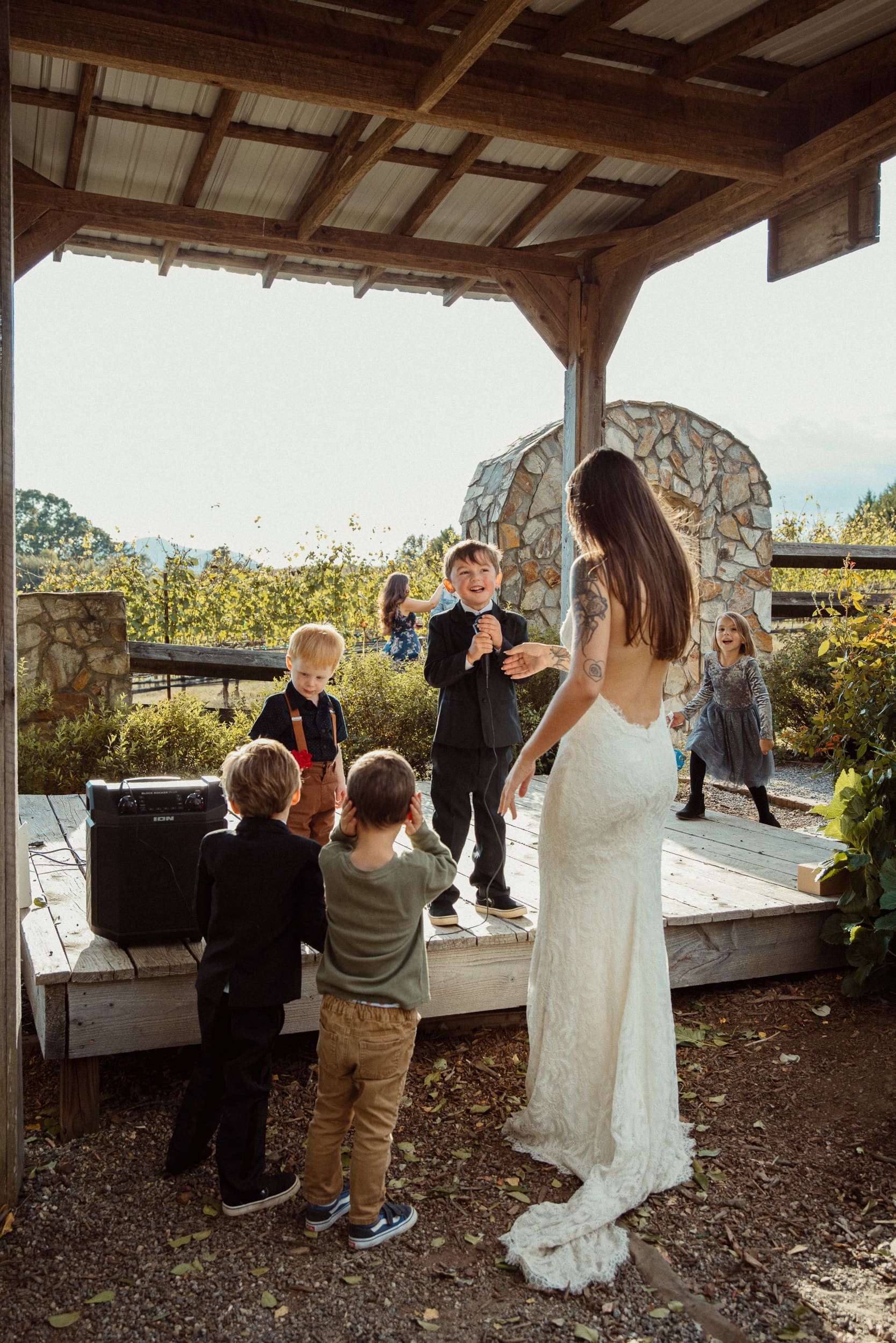 Bride surrounded by excited young children near stone arch at Parker-Binns Vineyard North Carolina wedding. 