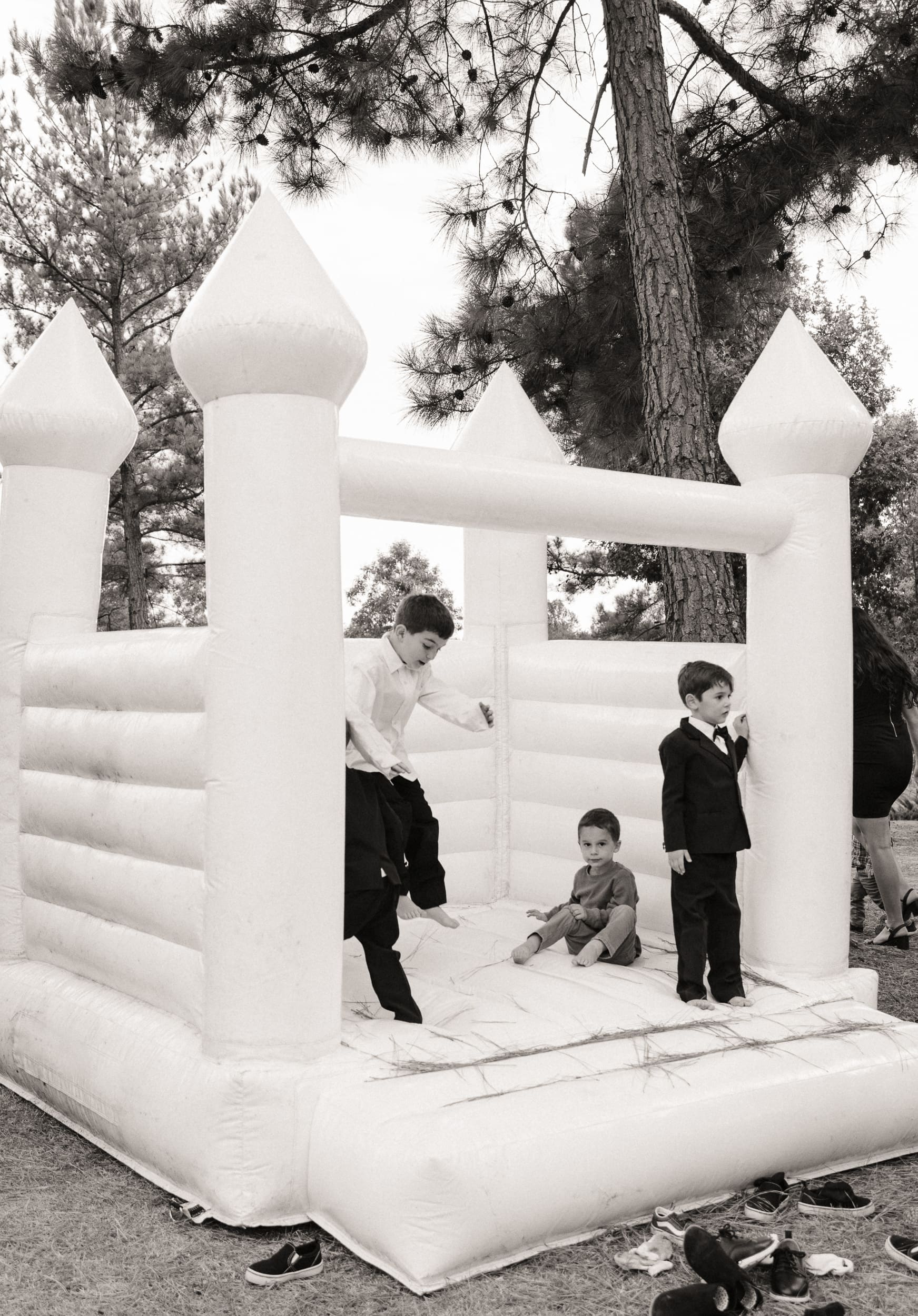 Children in suits playing in white bounce house at outdoor wedding reception, candid wedding photography by Brandi Denslow.