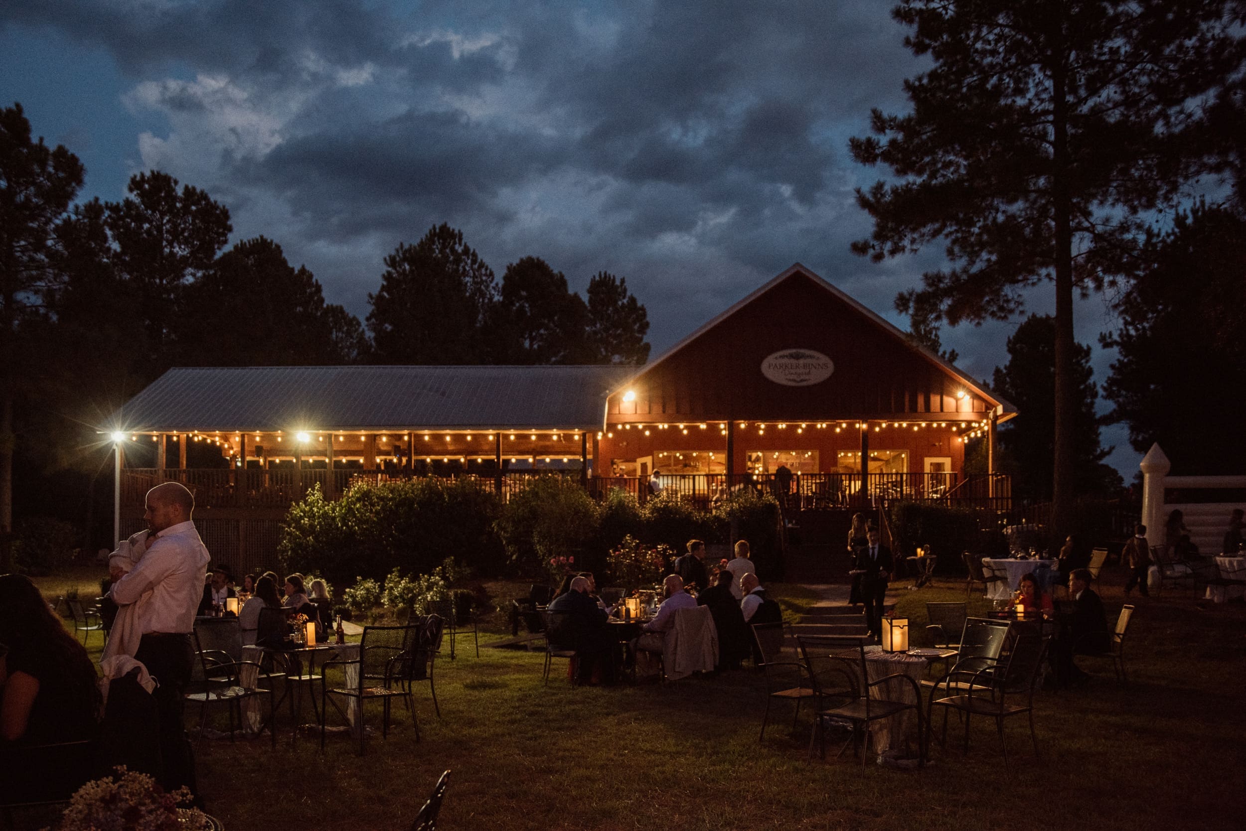 Parker-Binns Vineyard wedding venue lit up at night with string lights and guests dining under dramatic evening sky, North Carolina wedding photography Brandi Denslow. 