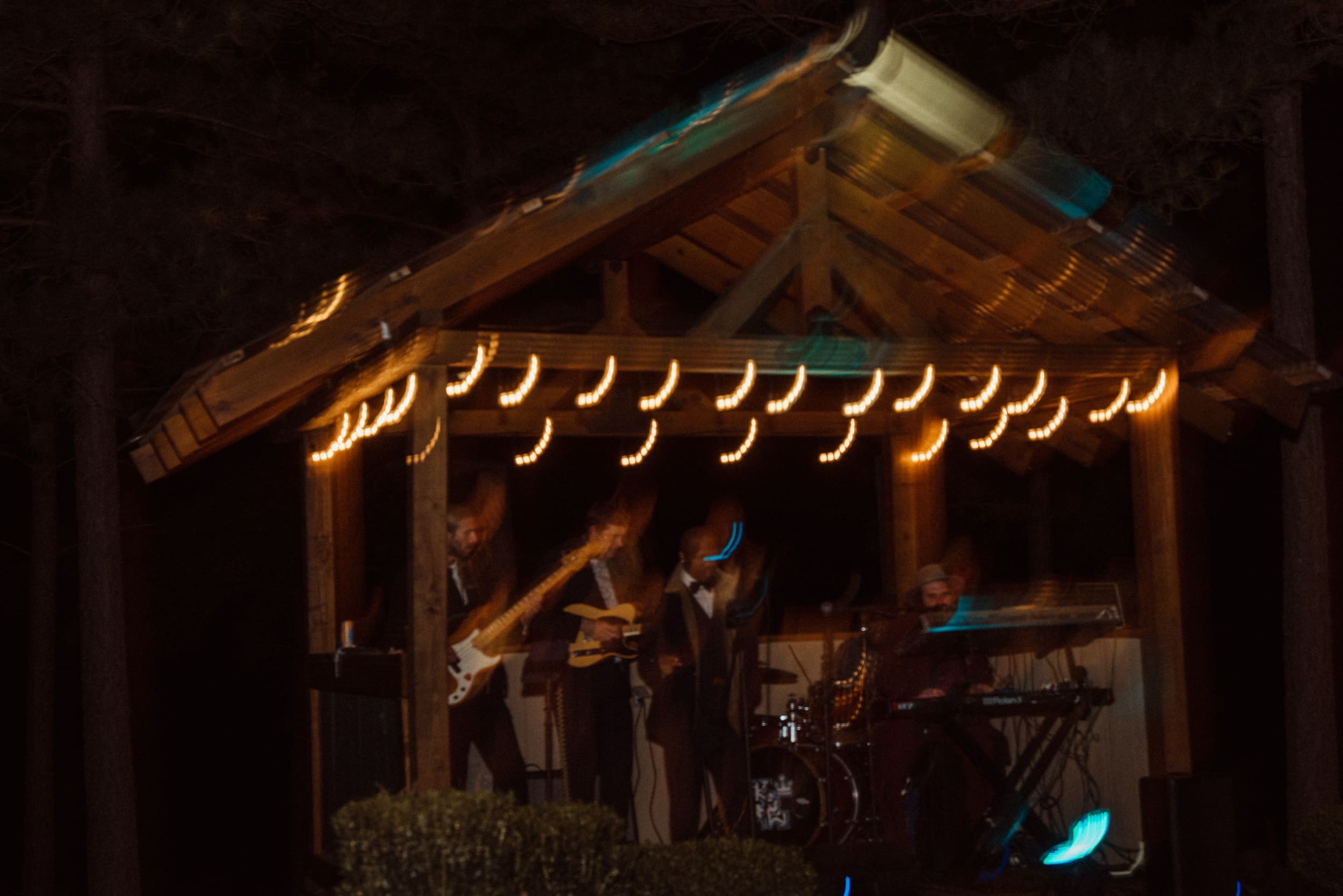 Live band performing under glowing pavilion with string lights at night during Parker-Binns Vineyard wedding reception. 