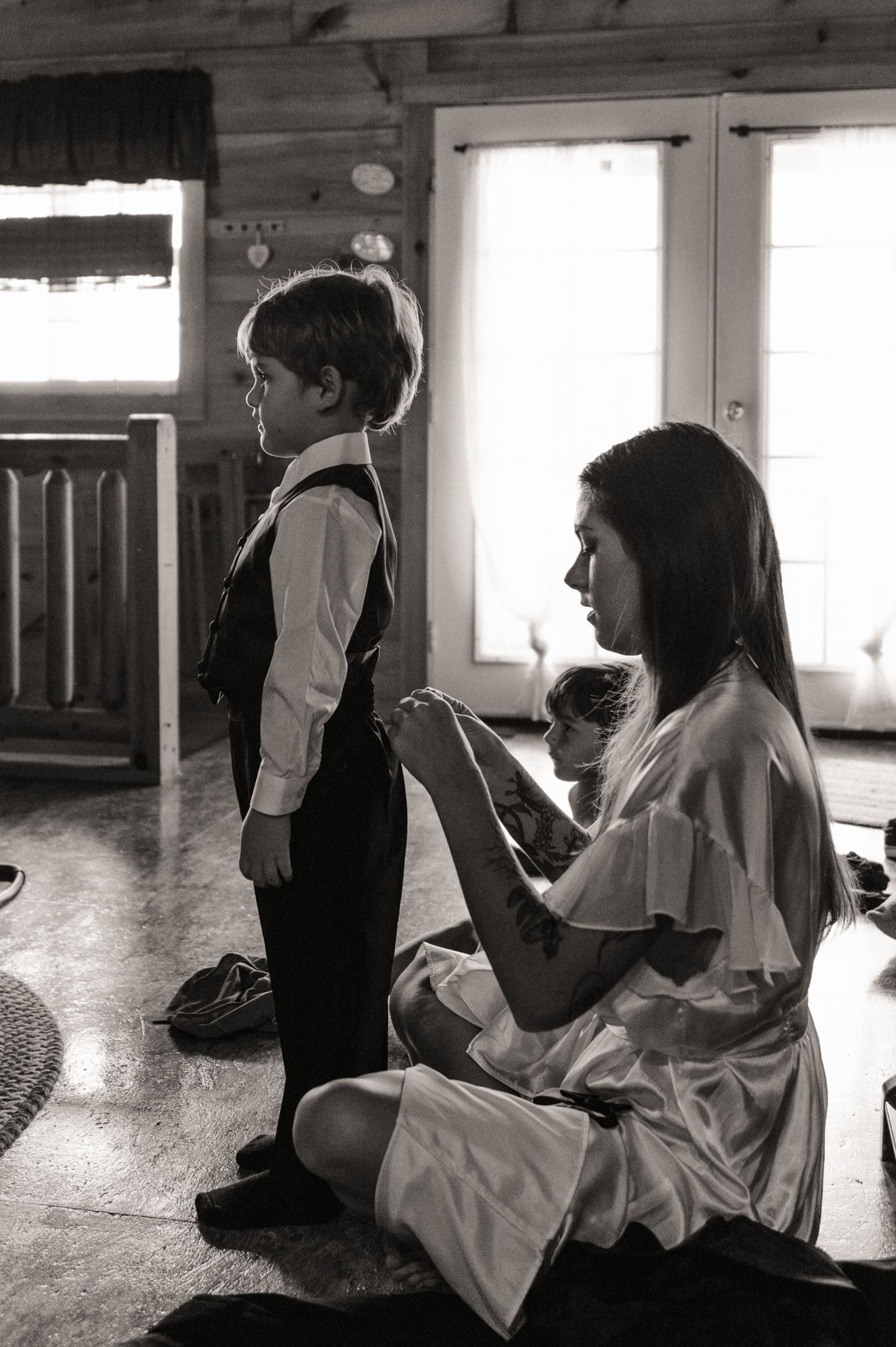 Black and white photo of bride in robe helping her young son with his suit jacket while getting ready at Parker-Binns Vineyard chateau.