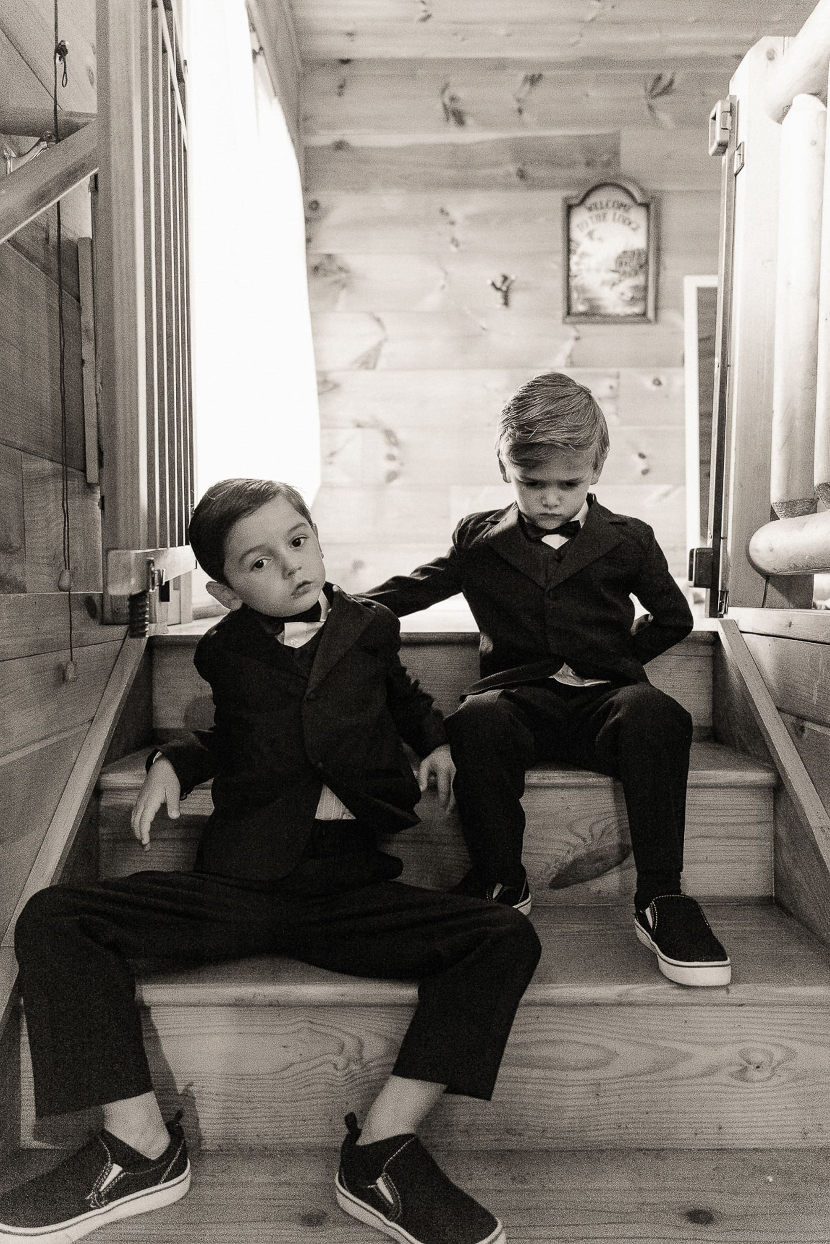 Tow young boys in suits sitting in a doorway at Parker-Binns Vineyard wedding, candid black and white photography by Brandi Denslow. 