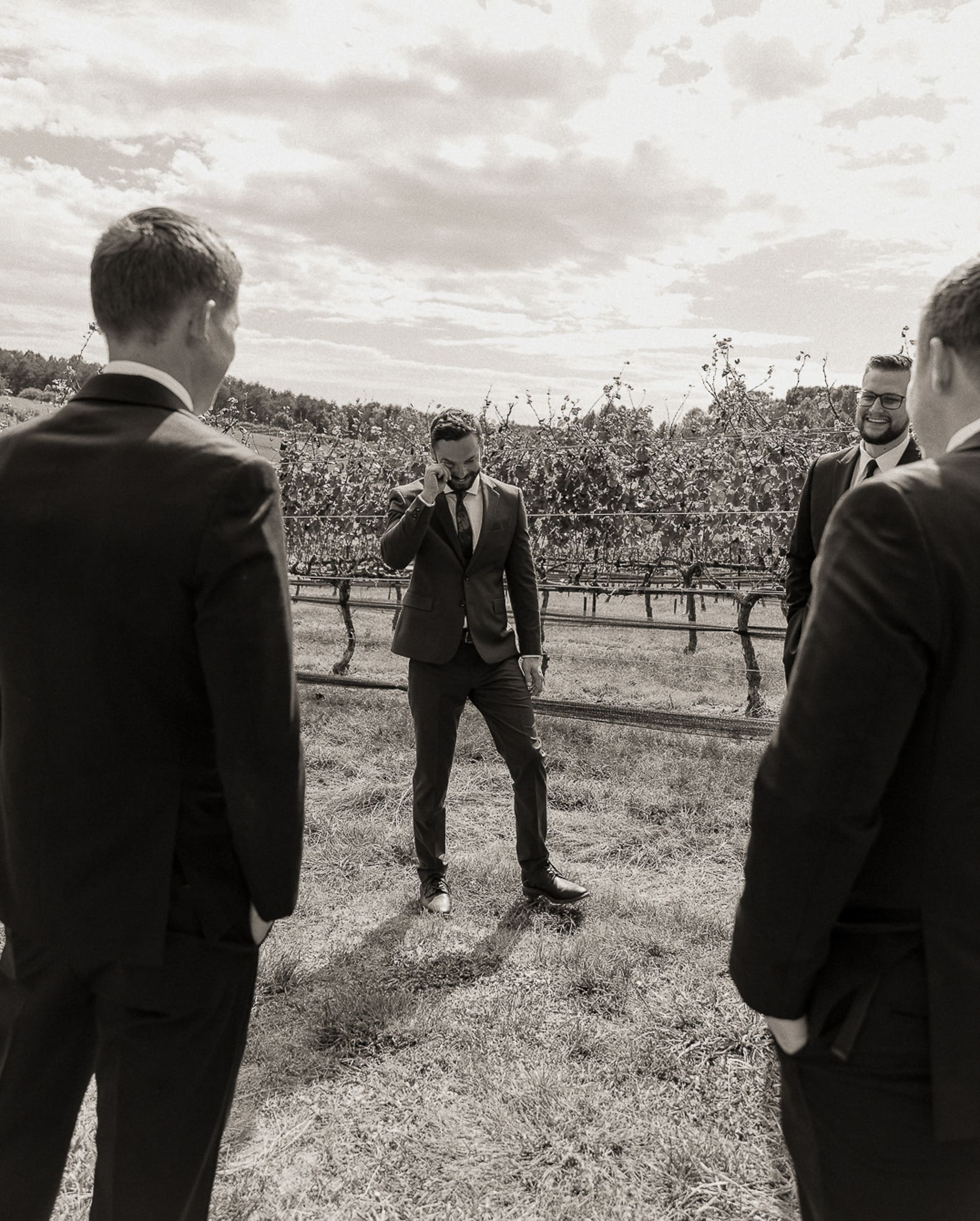 Groom and groomsmen at a destination North Carolina wedding having an emotional moment together as they stand among the vineyards.