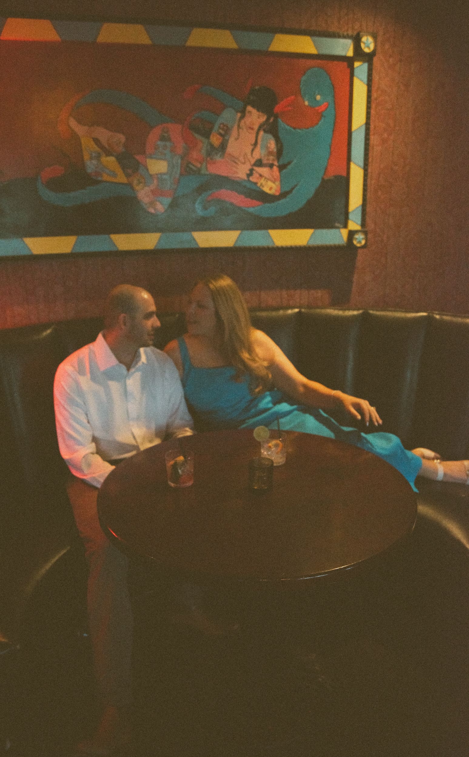 Engaged couple in a downtown bar booth during a St. Augustine night engagement session, photography by Brandi Denslow. 