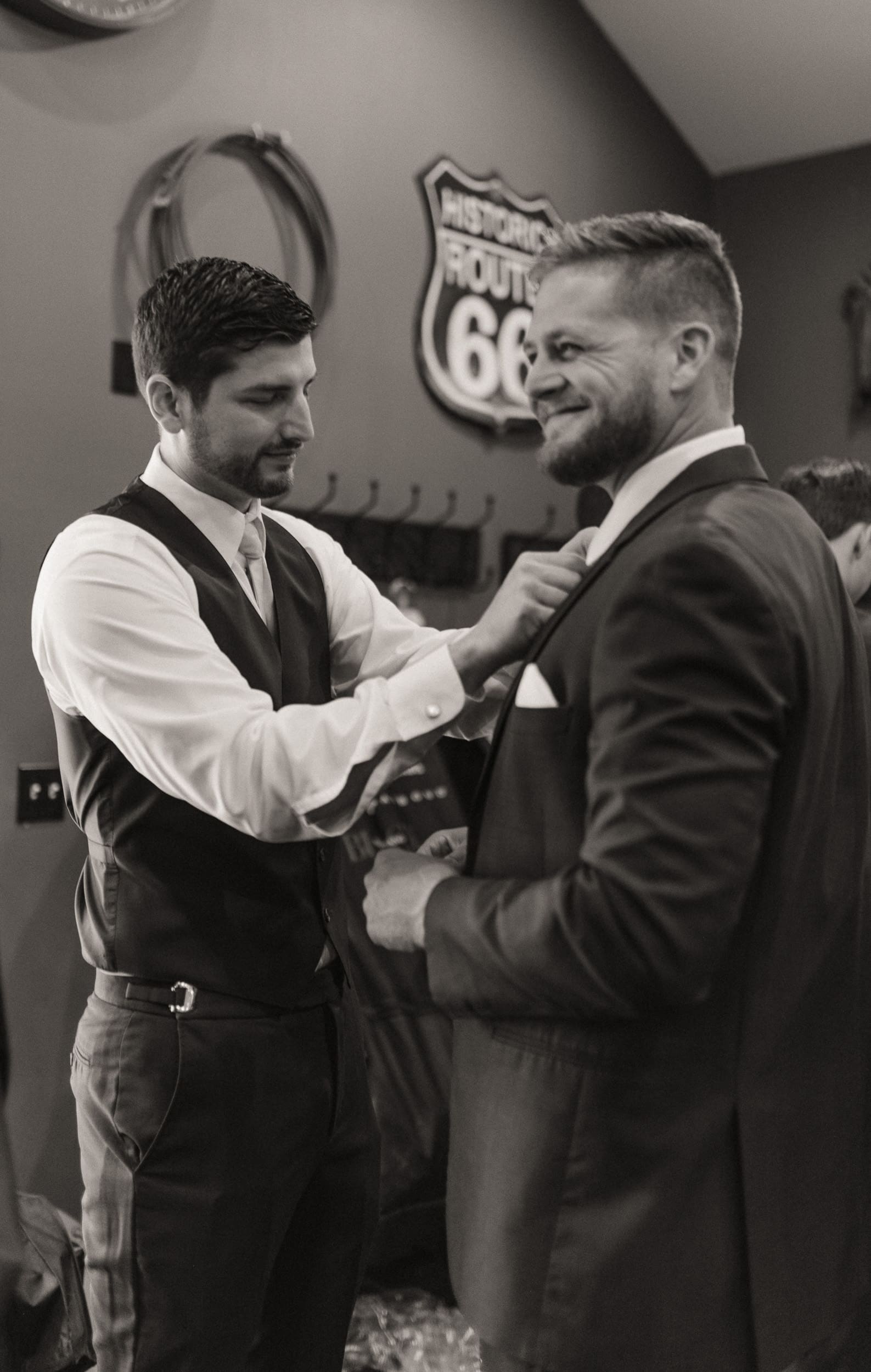 Groomsman helps the groom adjust his suit before the wedding ceremony. 