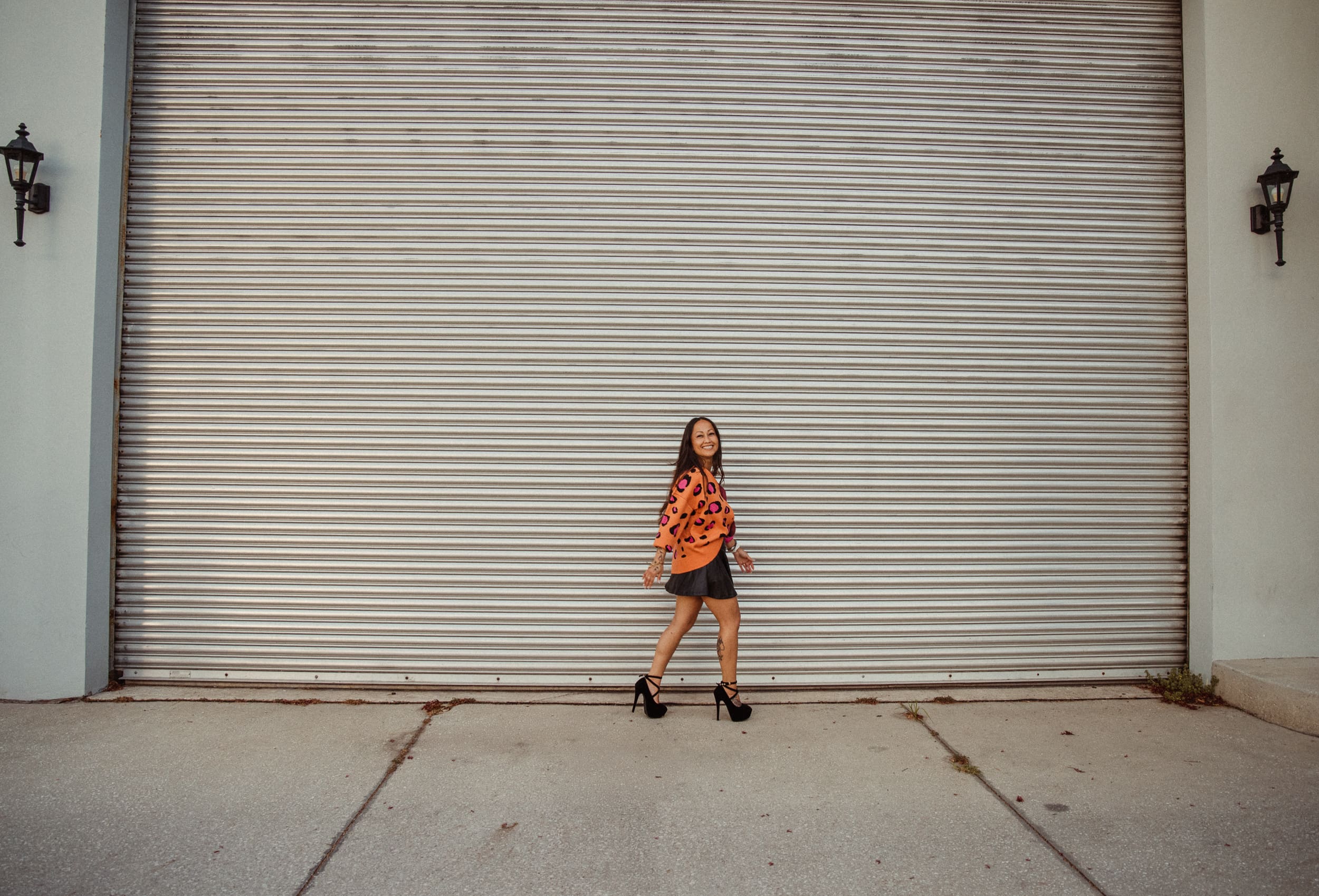 Woman in leopard print top walking in front of a corrugated garage door during a night photo shoot