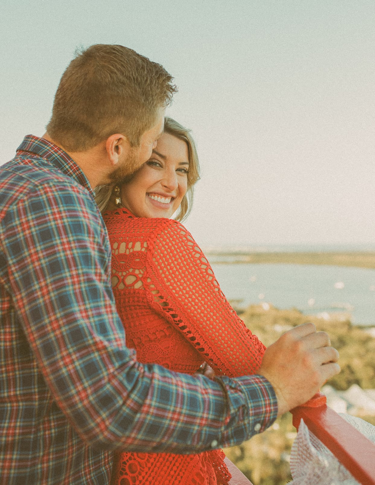 Man kissing his fiancée's cheek at the top of the St. Augustine Lighthouse with the marsh below