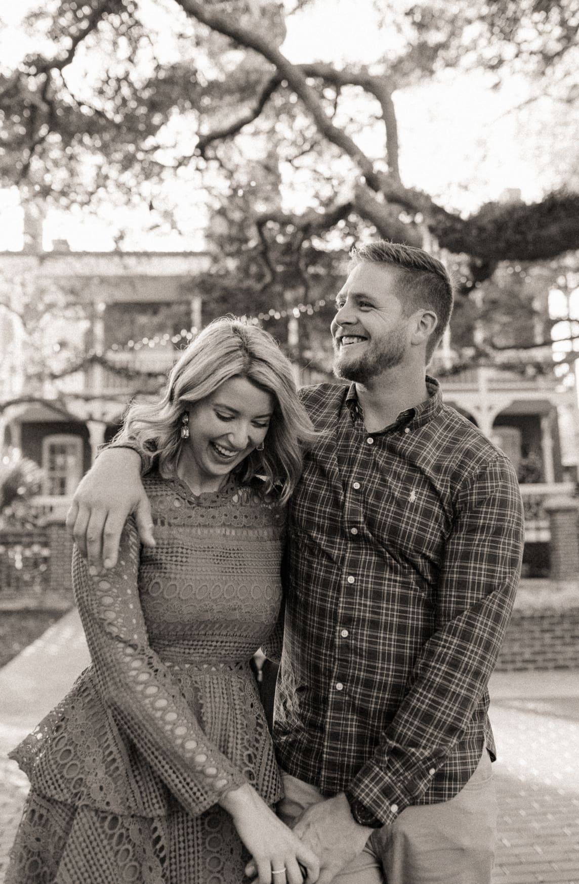 Black and white photo of an engaged couple laughing beneath live oak branches in St. Augustine