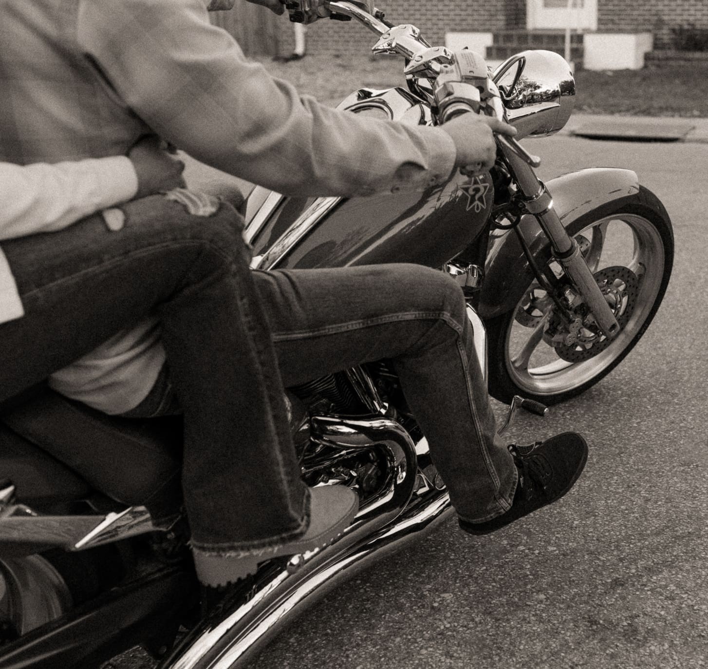  Black and white detail of hands on the handlebars and boots on the pegs of a motorcycle