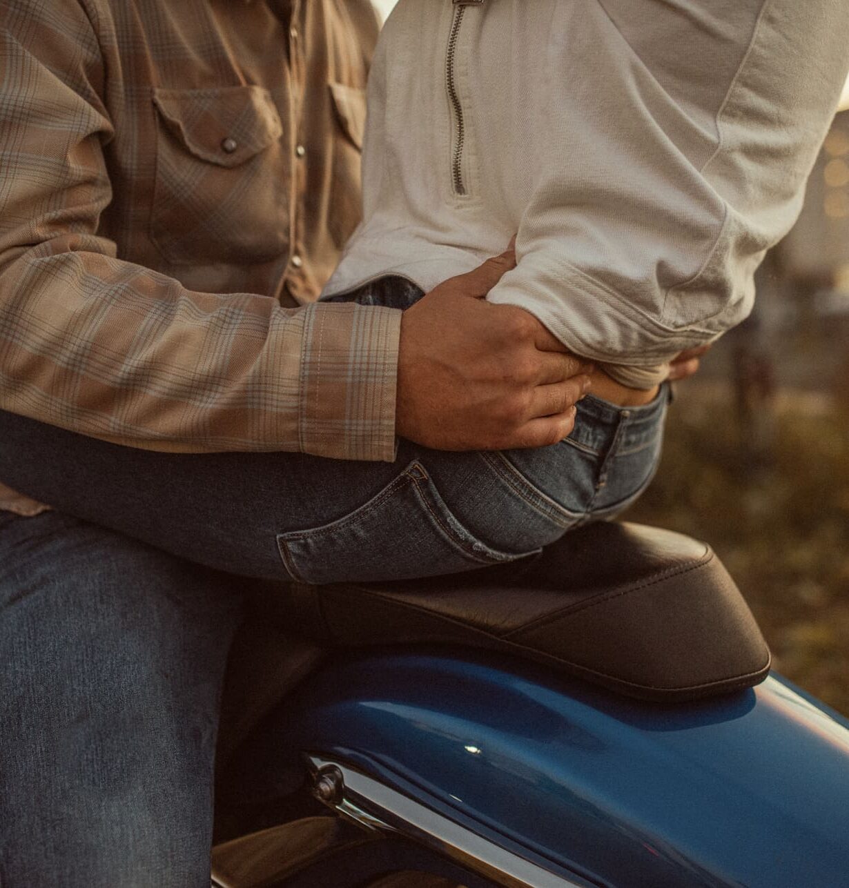 Detail of a man's hand resting on his fiancée's waist as they sit on a blue motorcycle