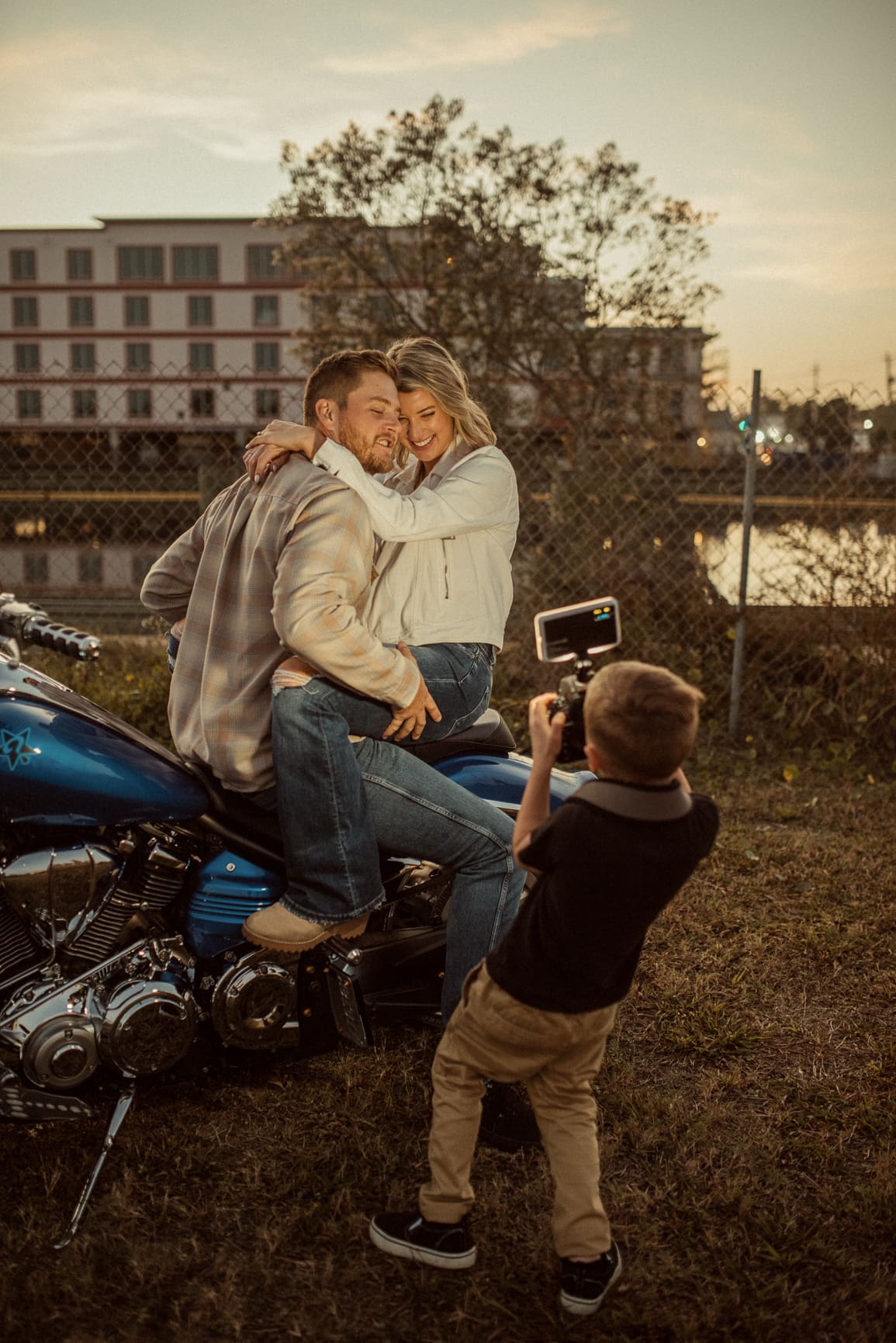  Boy photographing his dad and fiancée on a motorcycle by a chain-link fence in St. Augustine