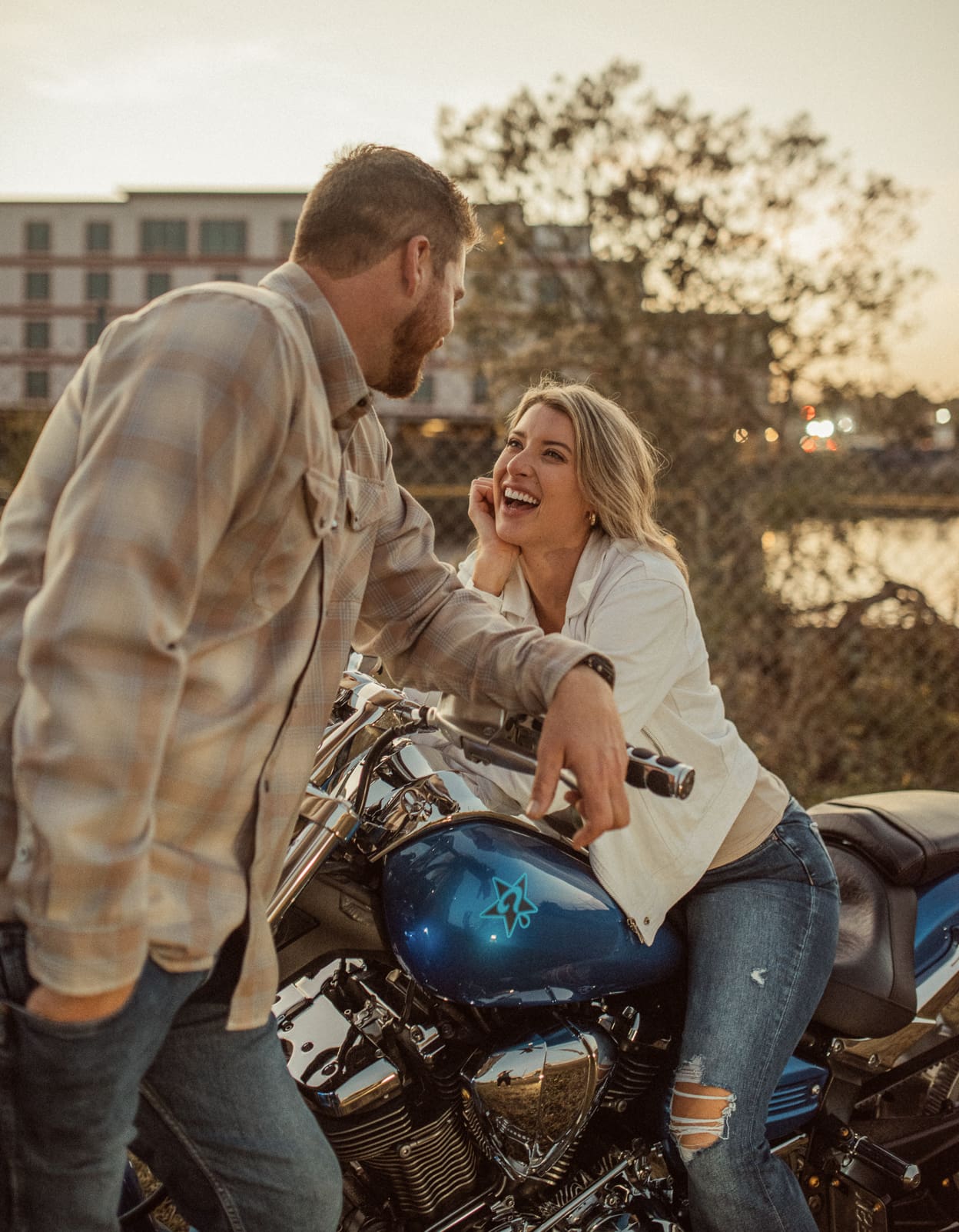 Woman laughing up at her fiancé while leaning on the handlebars of his motorcycle