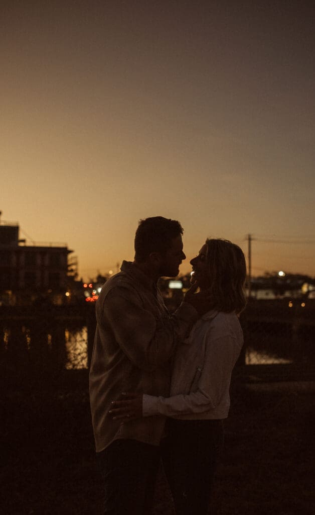  Silhouette of an engaged couple against a golden St. Augustine sunset with city lights on the water