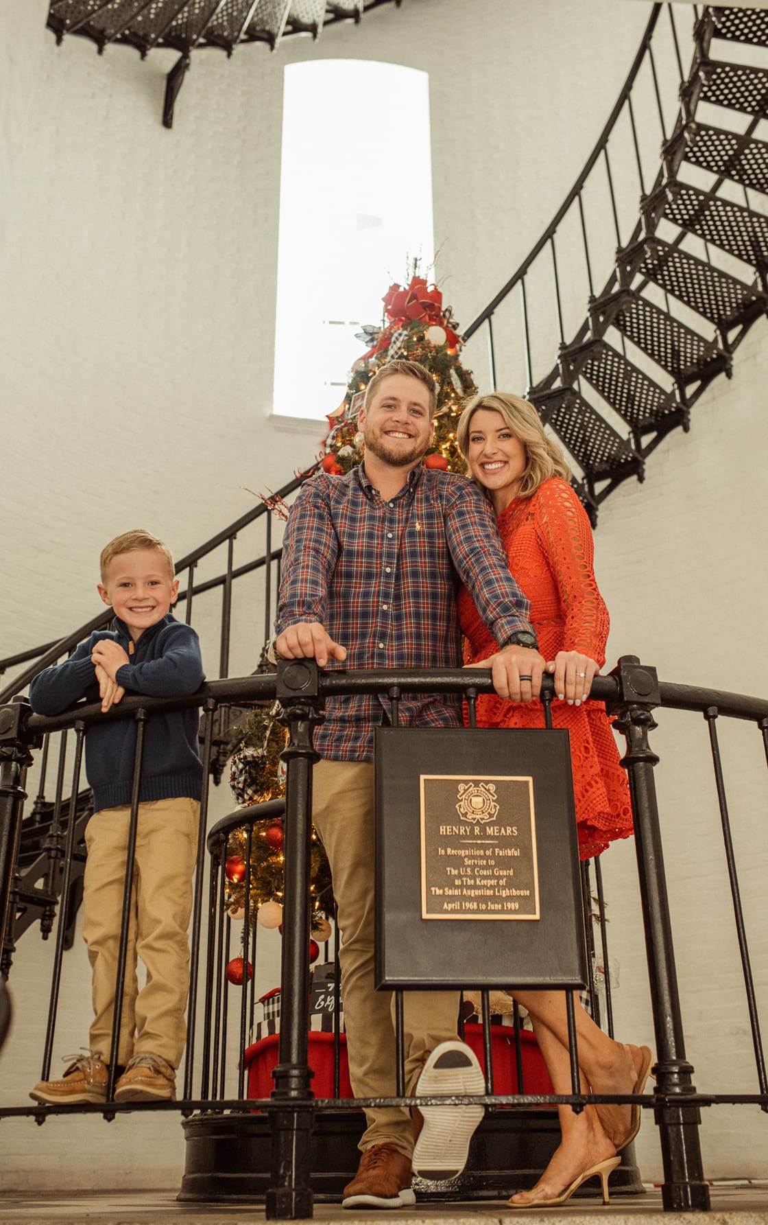 Family smiling at the railing inside the St. Augustine Lighthouse with a Christmas tree and spiral staircase behind them