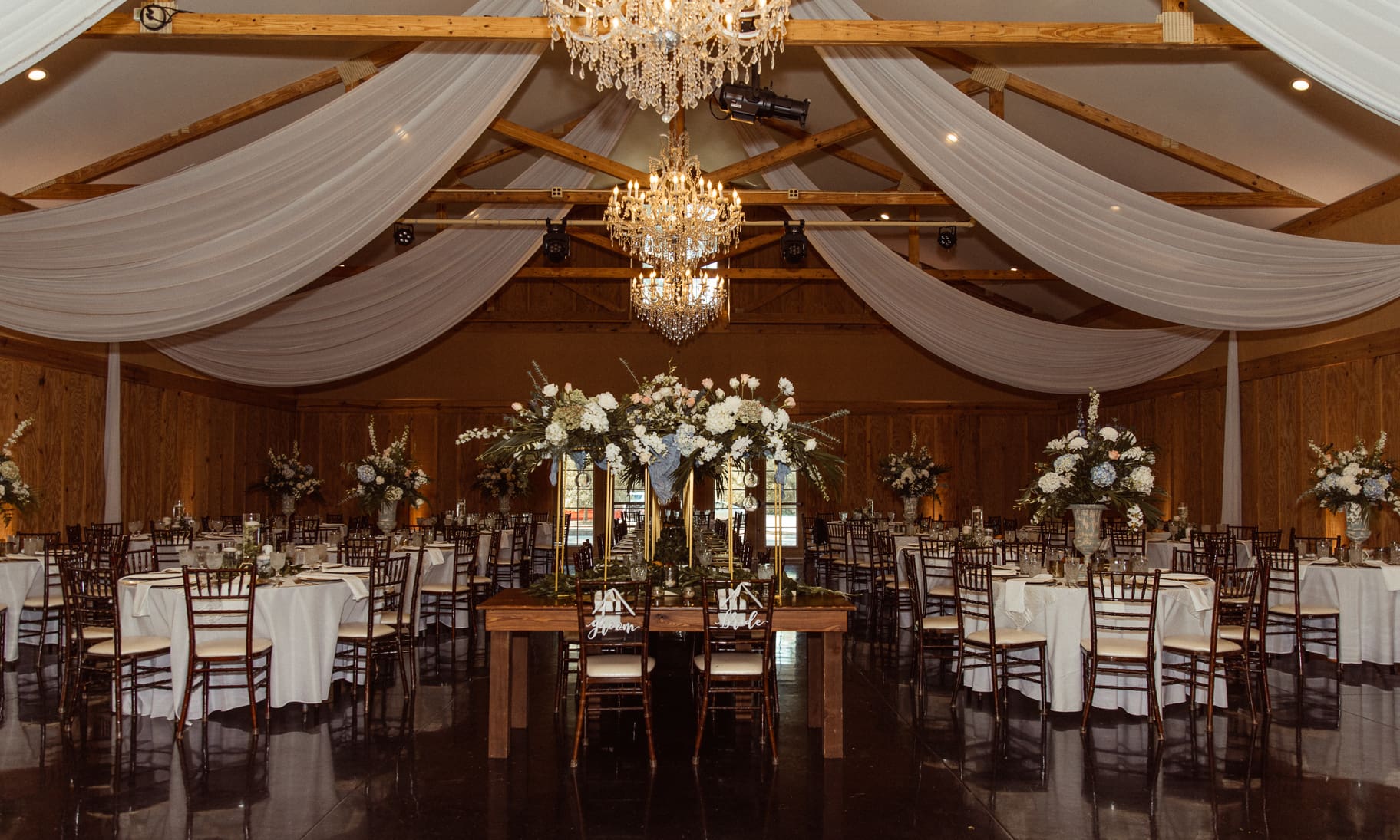 Bowing Oaks reception barn with crystal chandelier and tall floral centerpieces. 