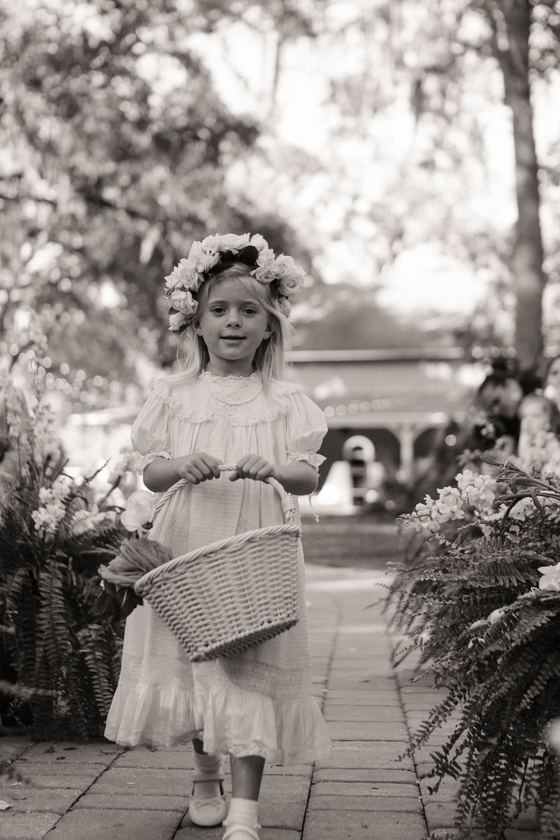 Flower girl holding a basket and wearing a flower crown, black and white wedding photo. 