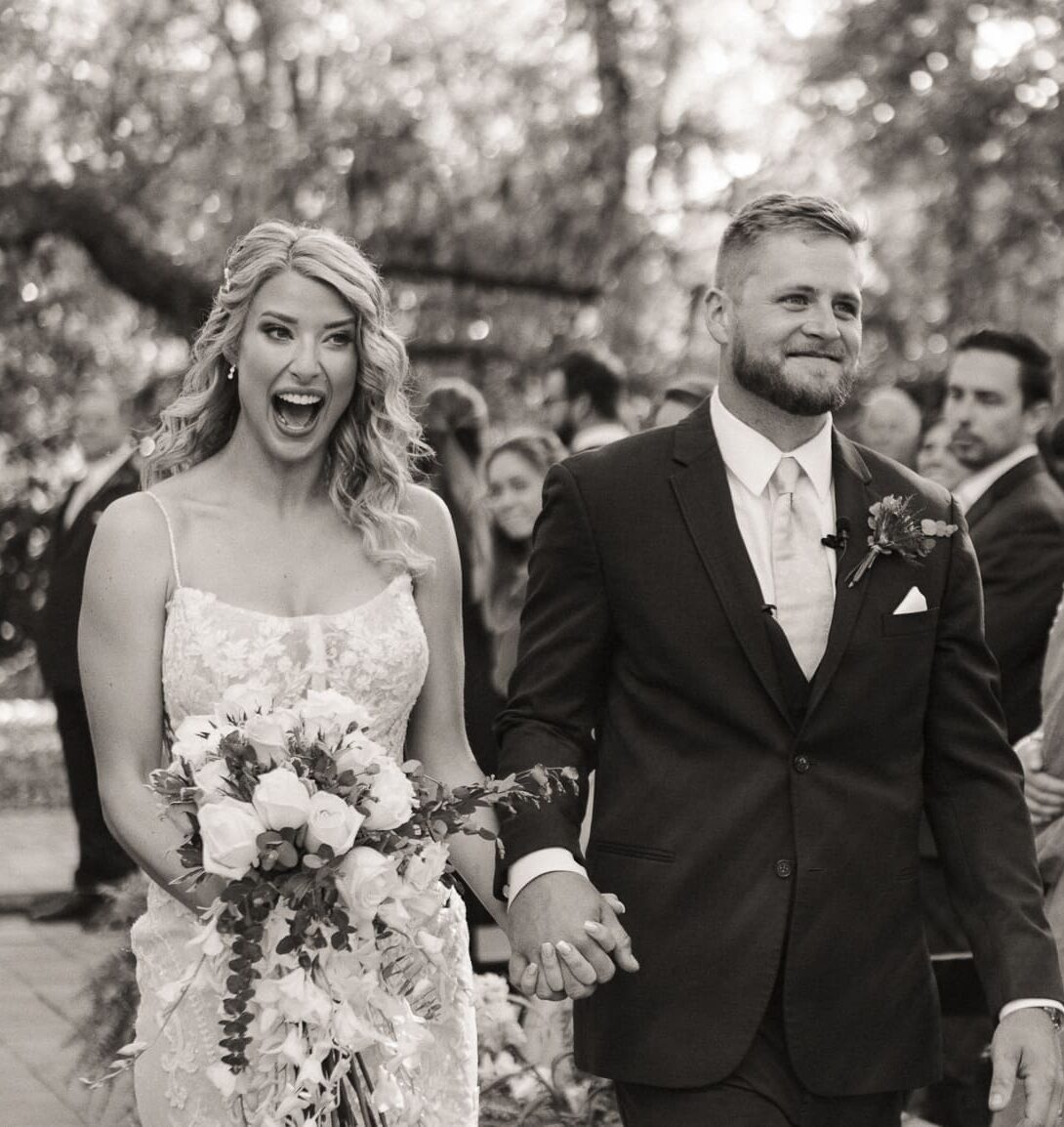 Bride laughing joyfully while holding groom's hand walking down the aisle at Bowing Oaks wedding. 