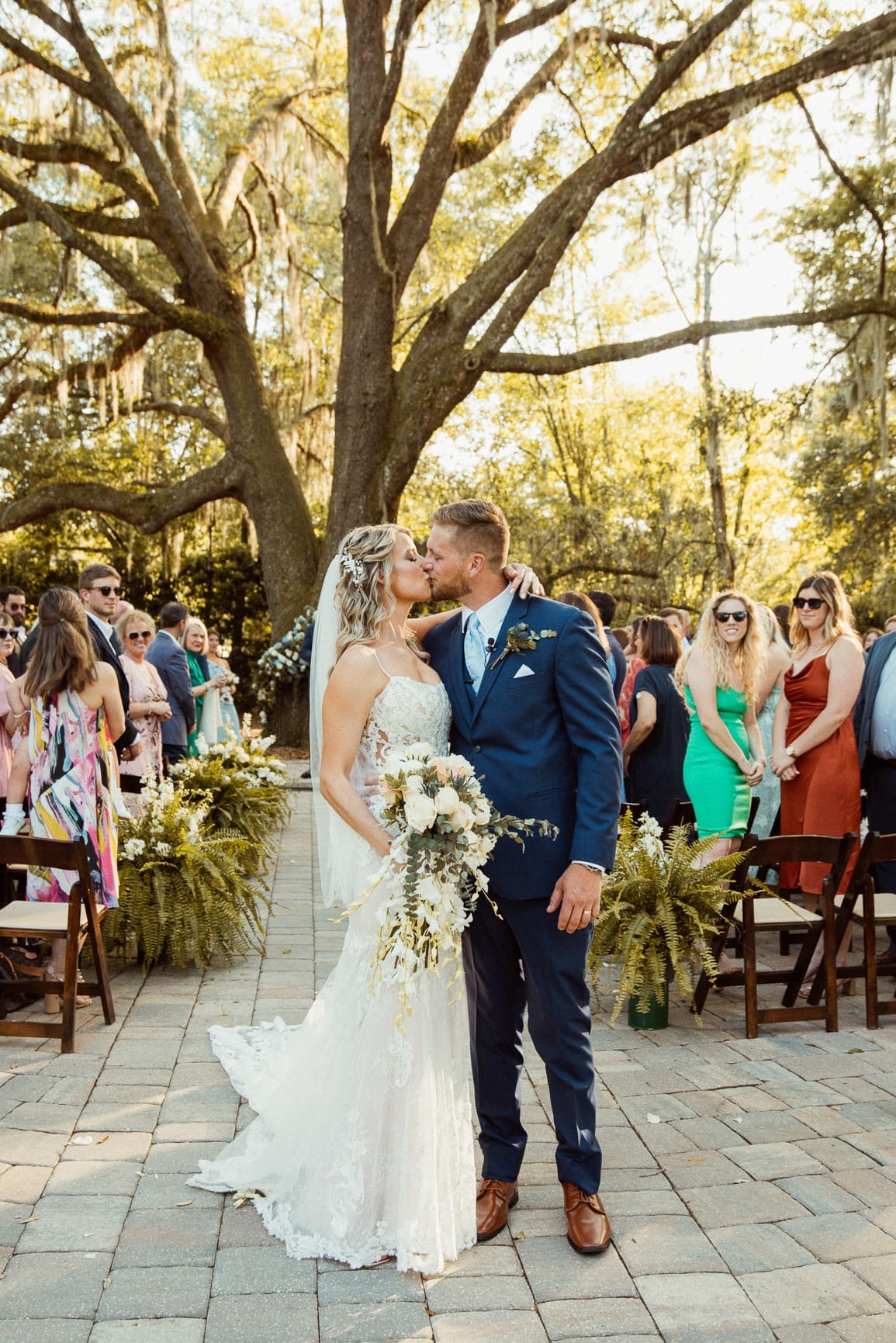 Bride and groom share first kiss under the iconic oak tree at Bowing Oaks wedding venue.